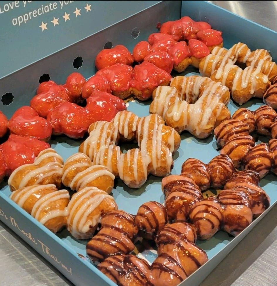 Box of assorted glazed and chocolate-drizzled pastries, including bright red ones, arranged in rows