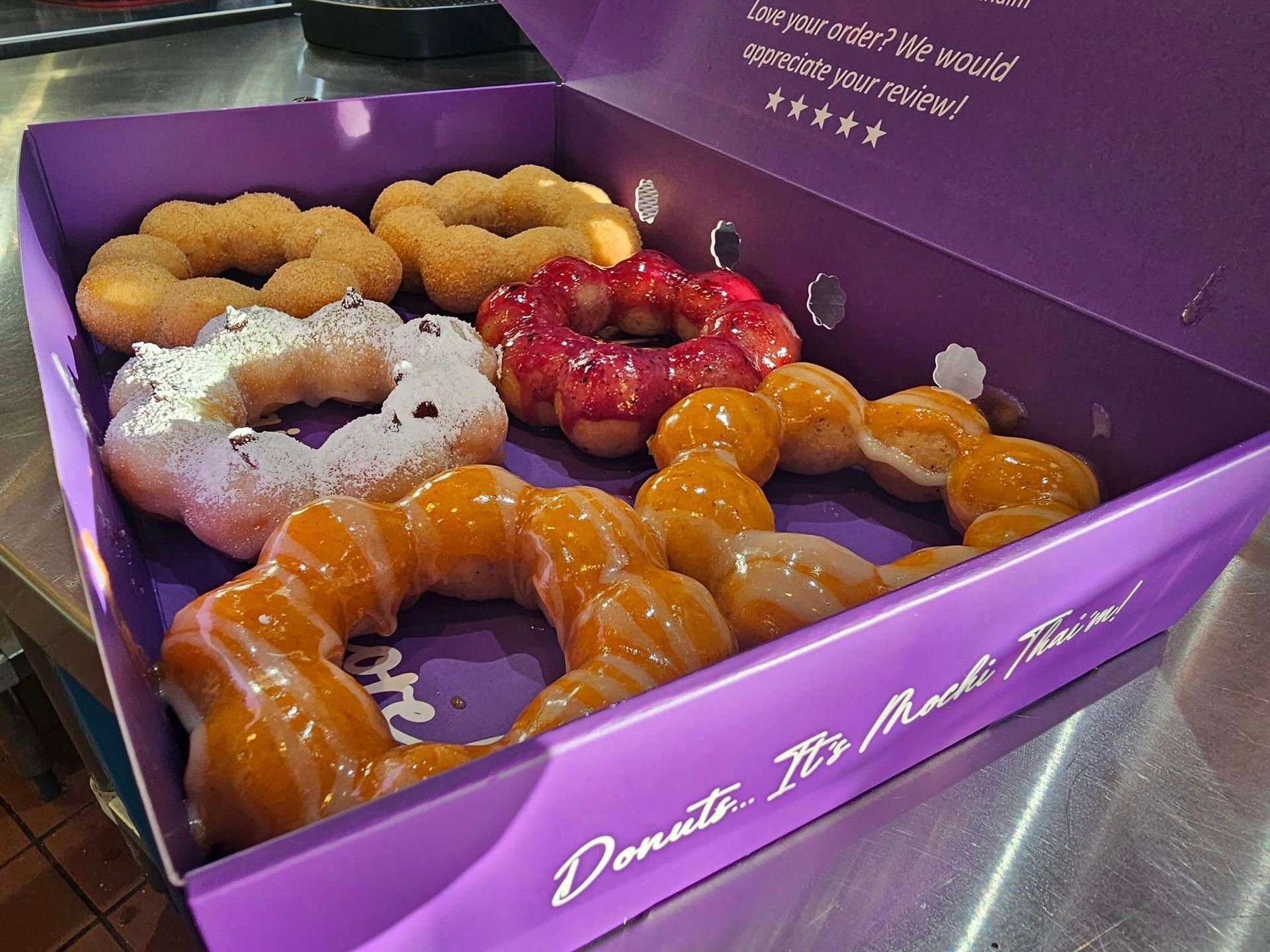 Assorted glazed donuts in a purple donut box on a table