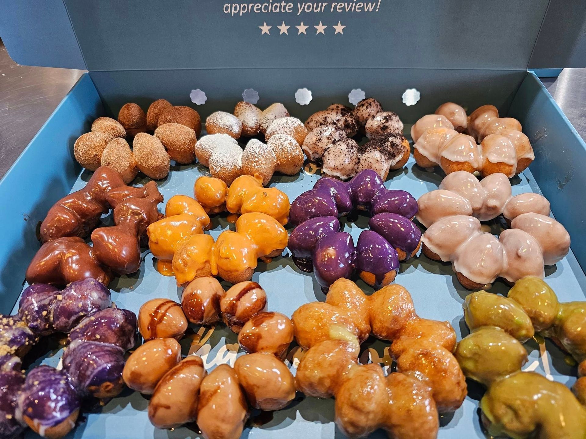 Assorted glazed mini pastries in a box, arranged in rows with assorted colors and toppings