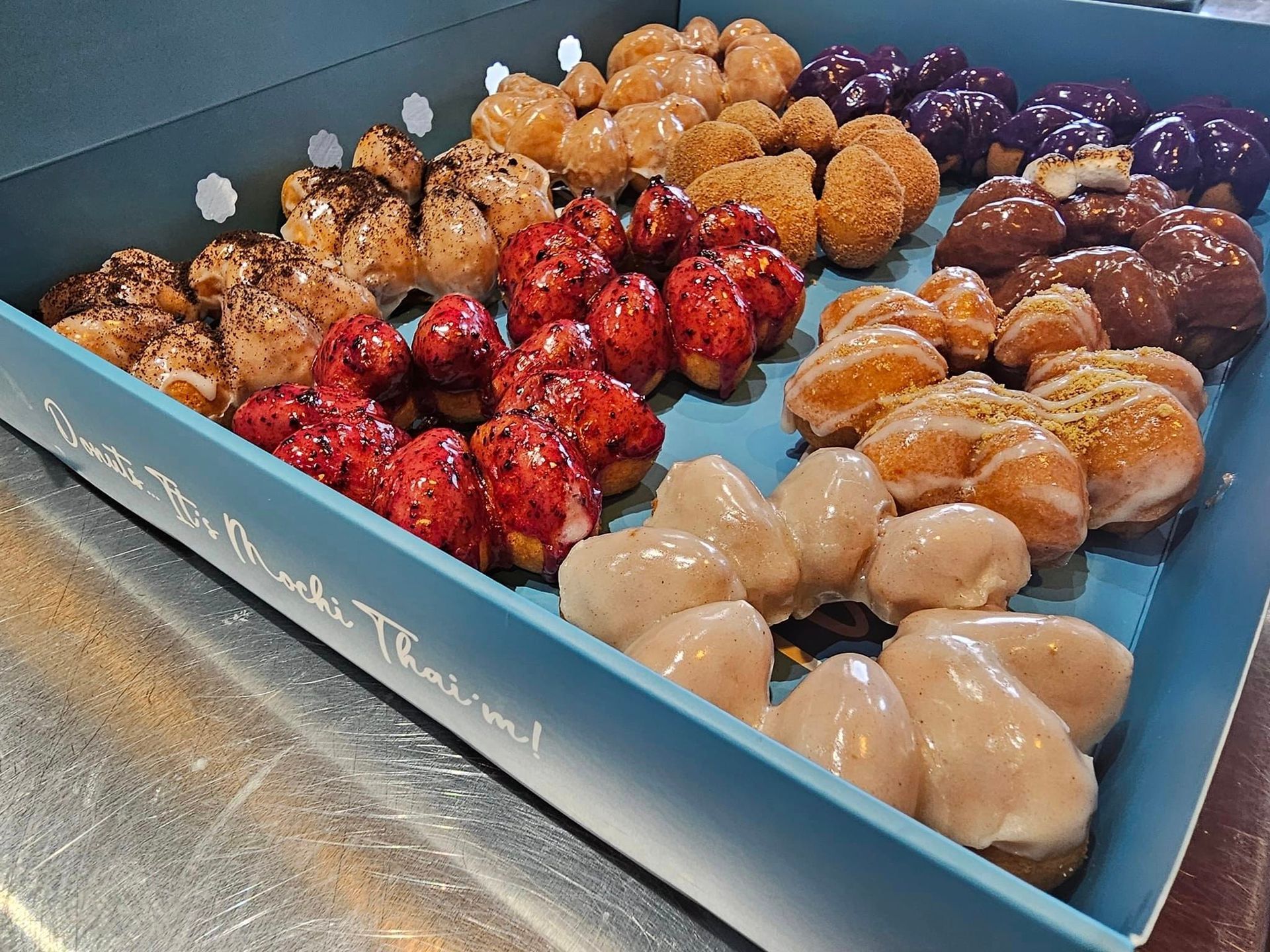 Assorted glazed doughnuts in a blue pastry box on a stainless steel counter
