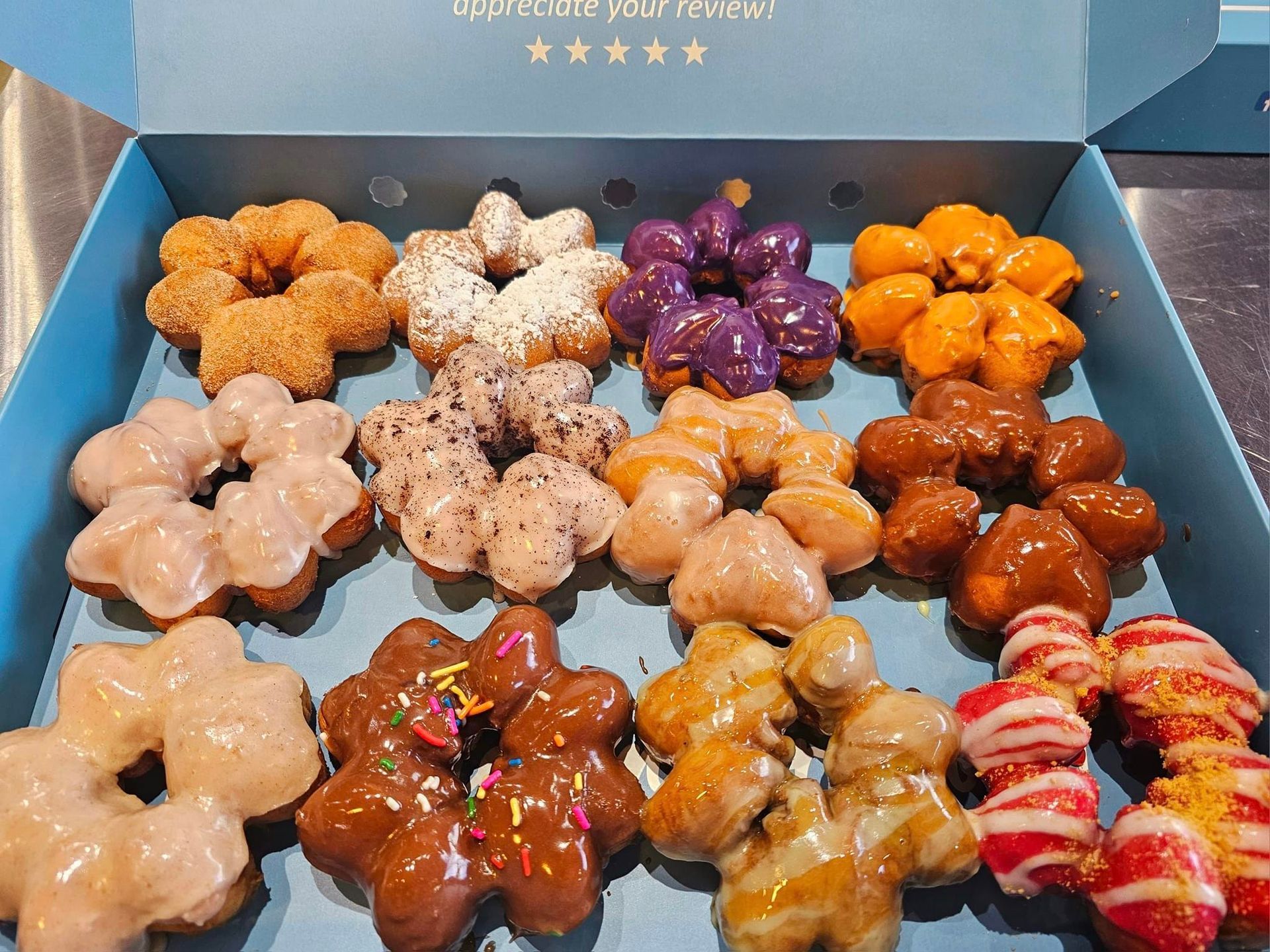 Assorted glazed pastries arranged in a blue box, in beige, purple, orange, and red swirls.