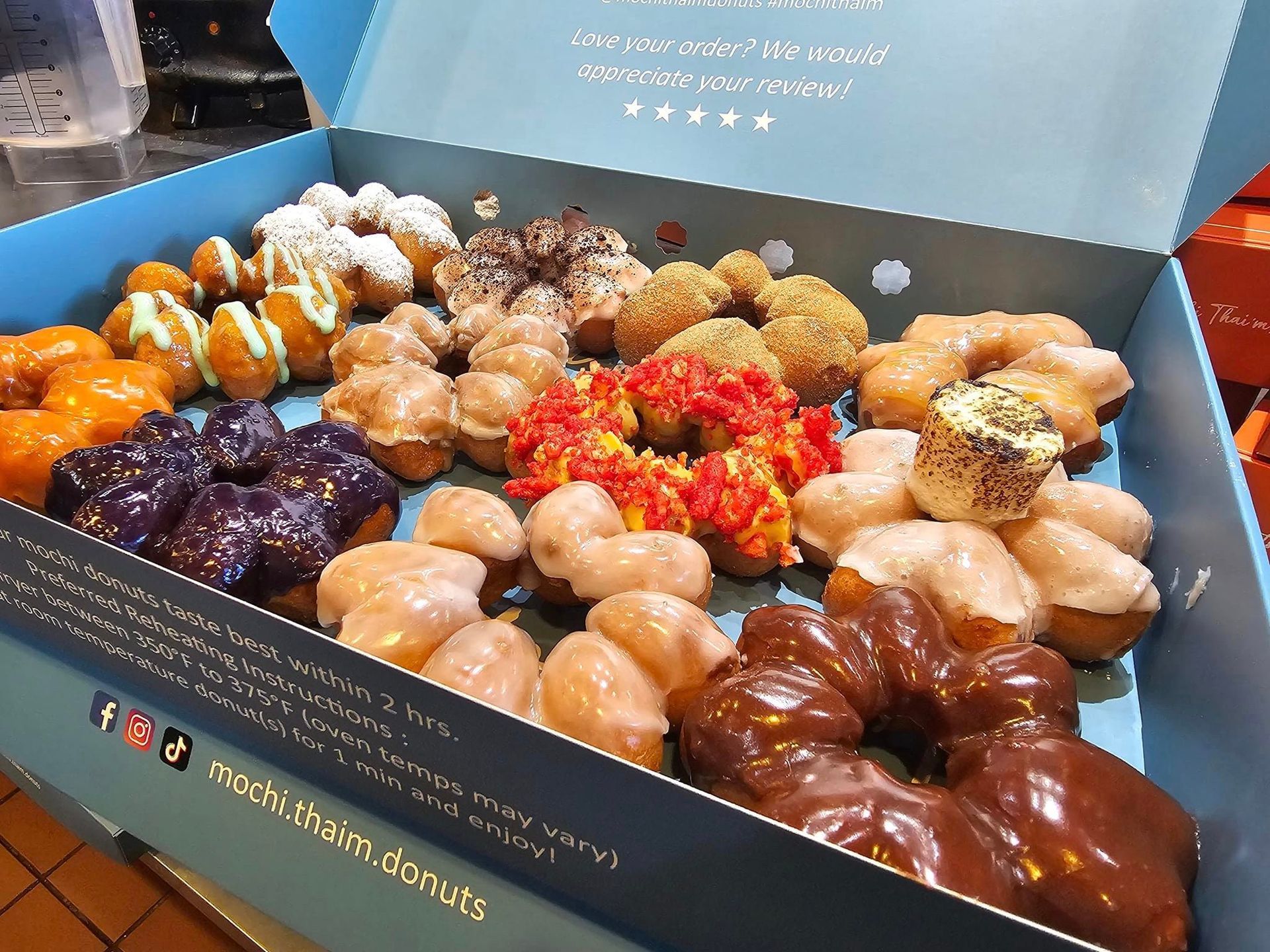 Assorted glazed donuts and pastries in an open bakery box, with colorful toppings and sprinkles.