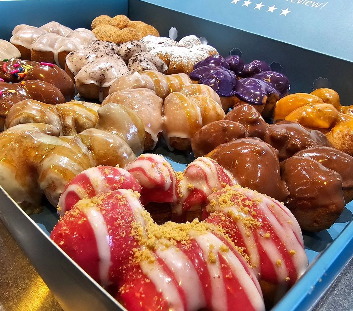 Tray of assorted glazed donuts, including pink and chocolate frosted varieties, arranged in rows