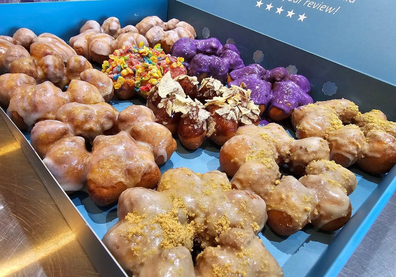 Tray of assorted glazed donuts with colorful toppings on a bakery display counter