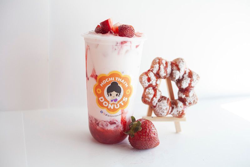 Strawberry dessert drink with whipped cream, donuts, and fresh strawberries on a white surface