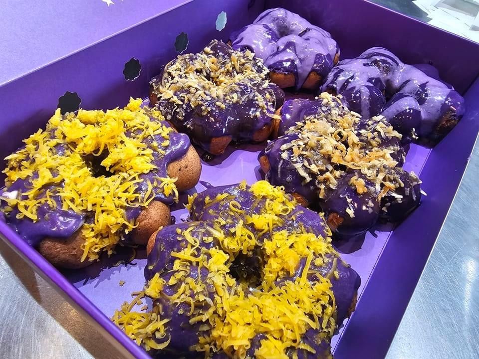 Purple tray of donuts topped with yellow and purple icing and sprinkles