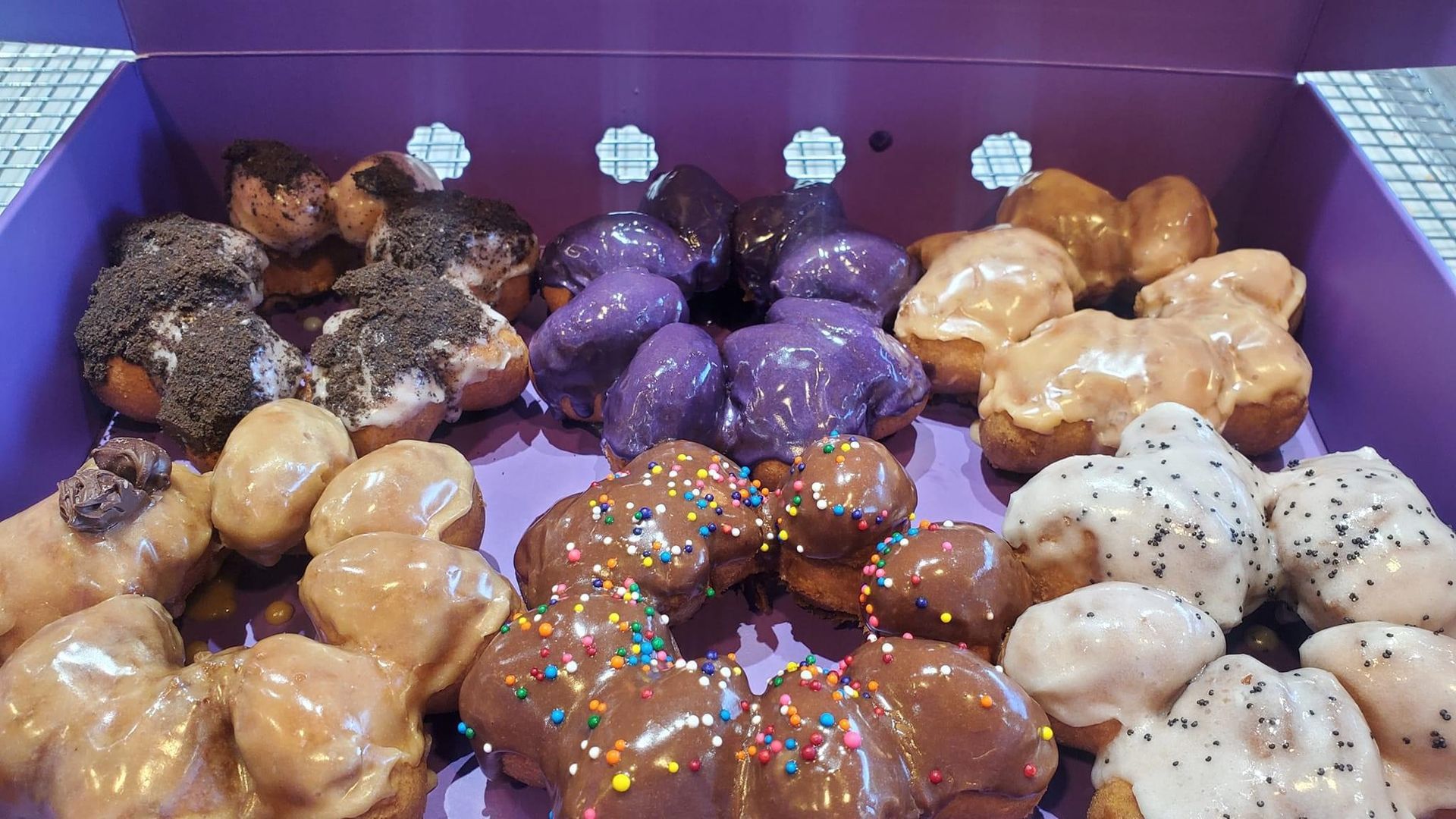 Assorted glazed donuts with colorful sprinkles in a purple box