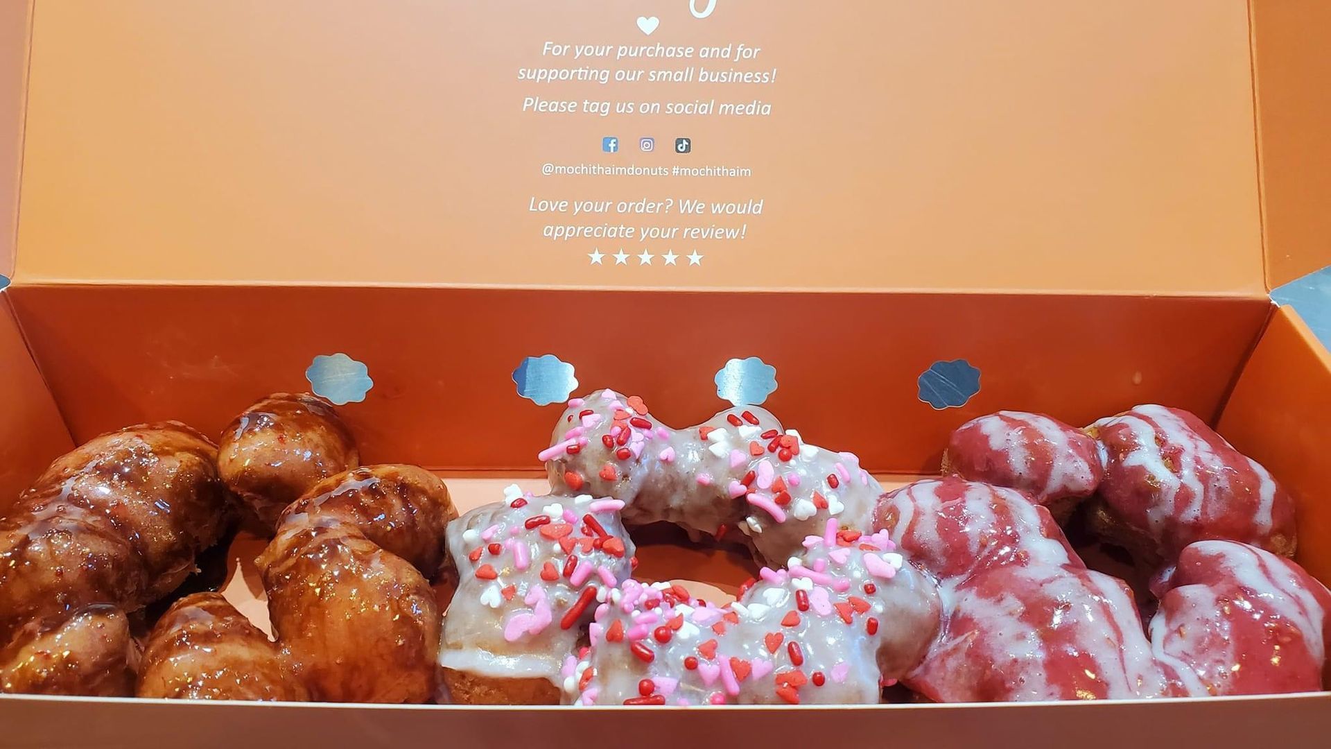 Assorted glazed and sprinkled donuts in an orange bakery box