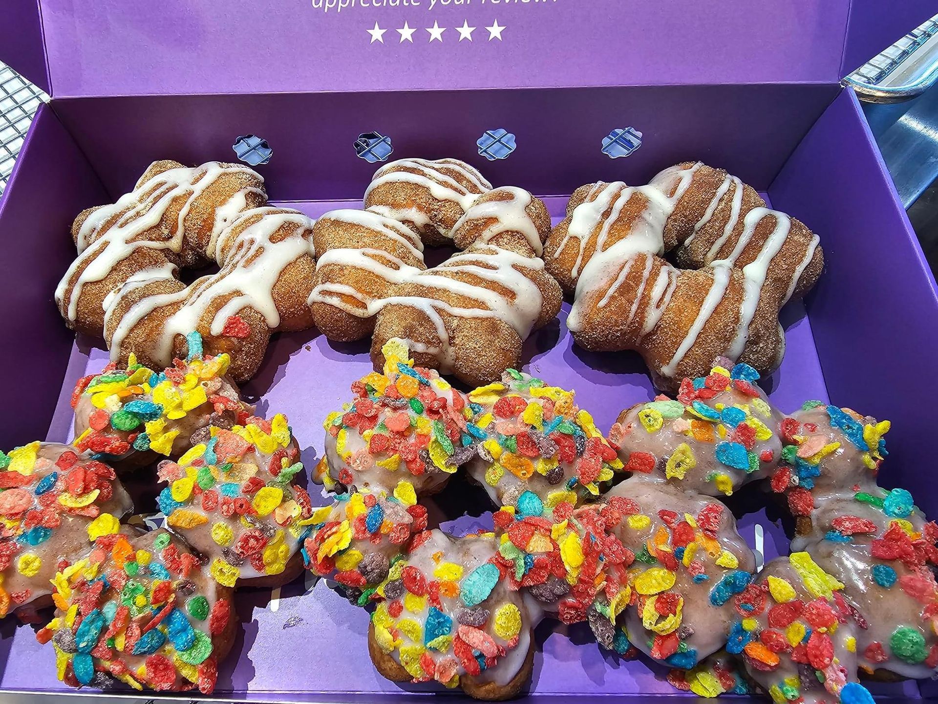 Box of assorted pastries and colorful cereal-topped donuts on a purple tray