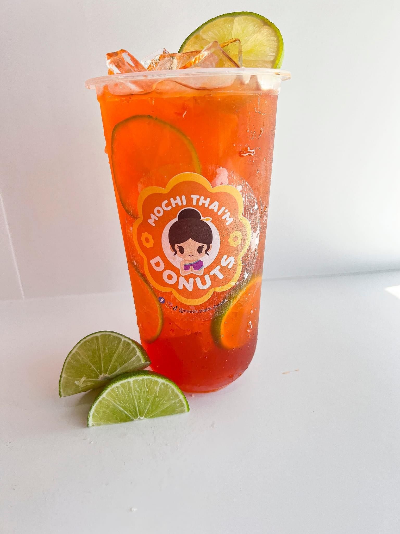 Orange slush drink in a clear cup with lime slices and crushed ice, on a white background