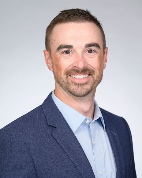 Professional headshot of a smiling person in a blue blazer and light blue shirt on a neutral background