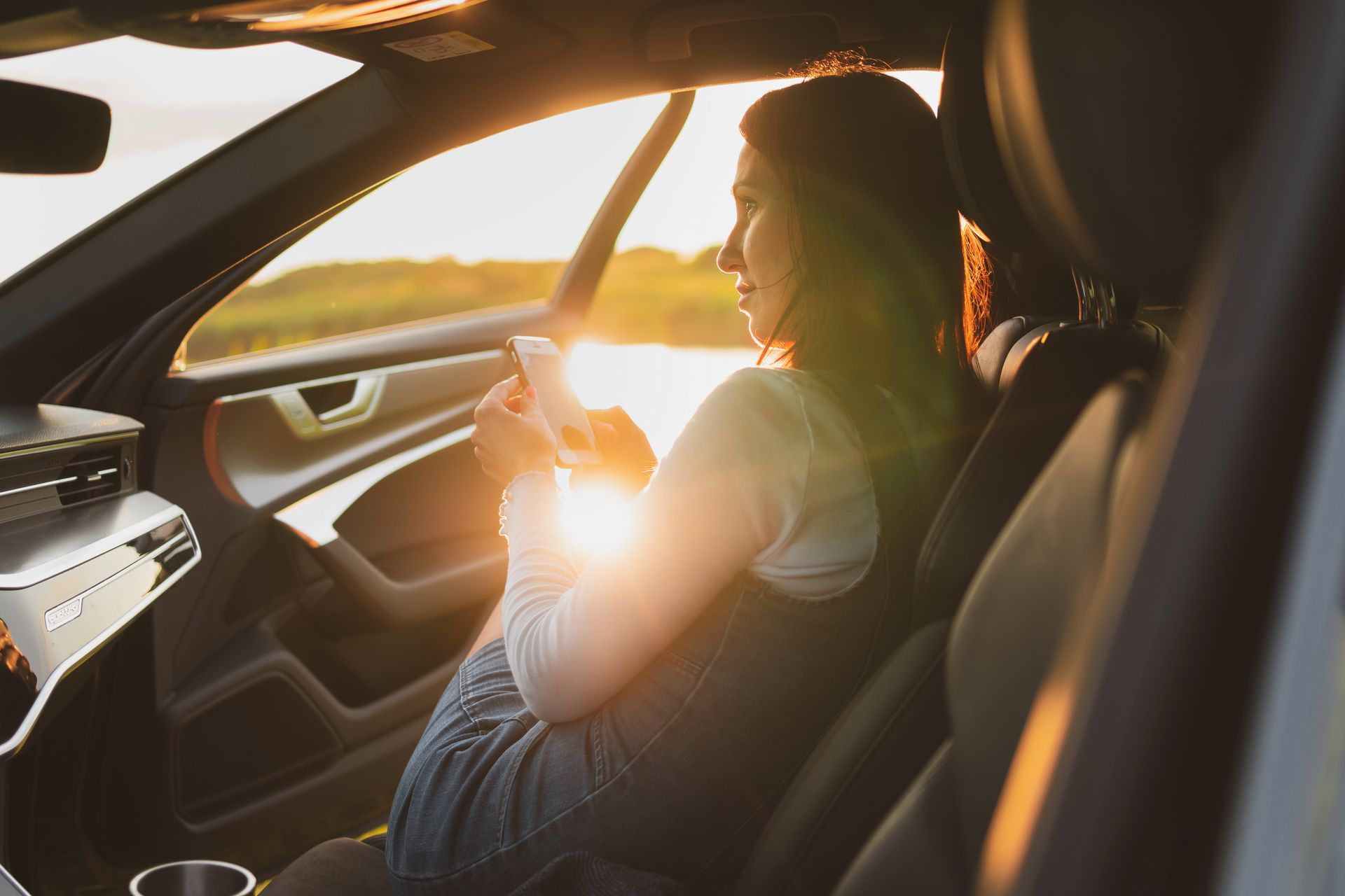 Person sitting in a car at sunset, holding a phone with sunlight streaming through the window
