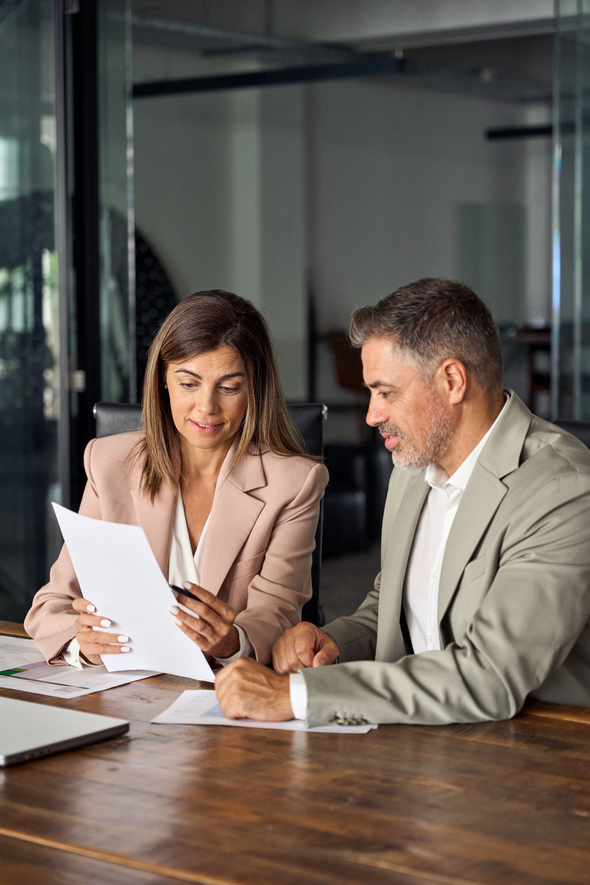 Two colleagues reviewing a document at a conference table in a glass-walled office