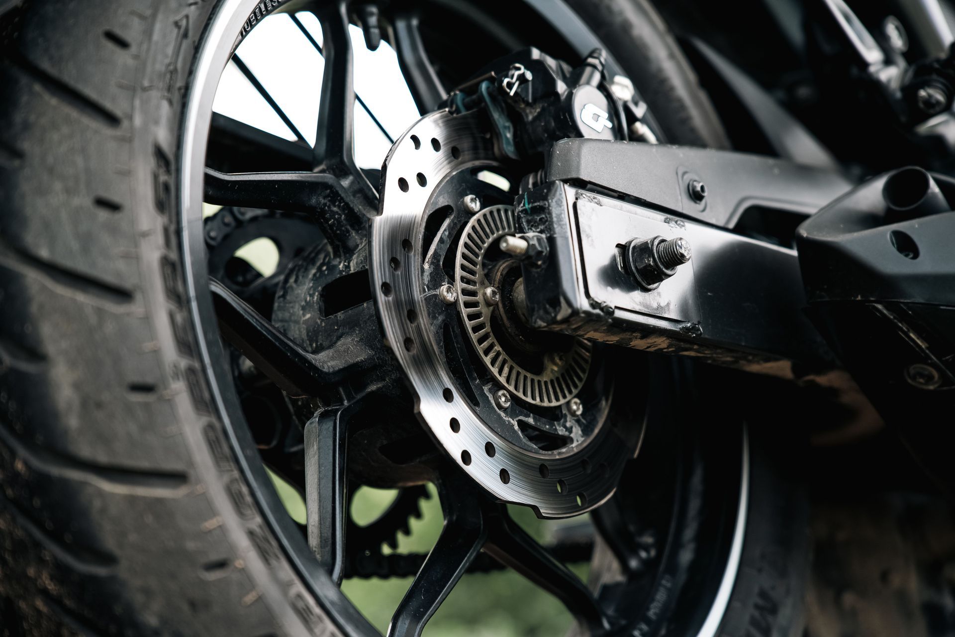 Close-up of a motorcycle rear wheel and disc brake assembly with black and silver components