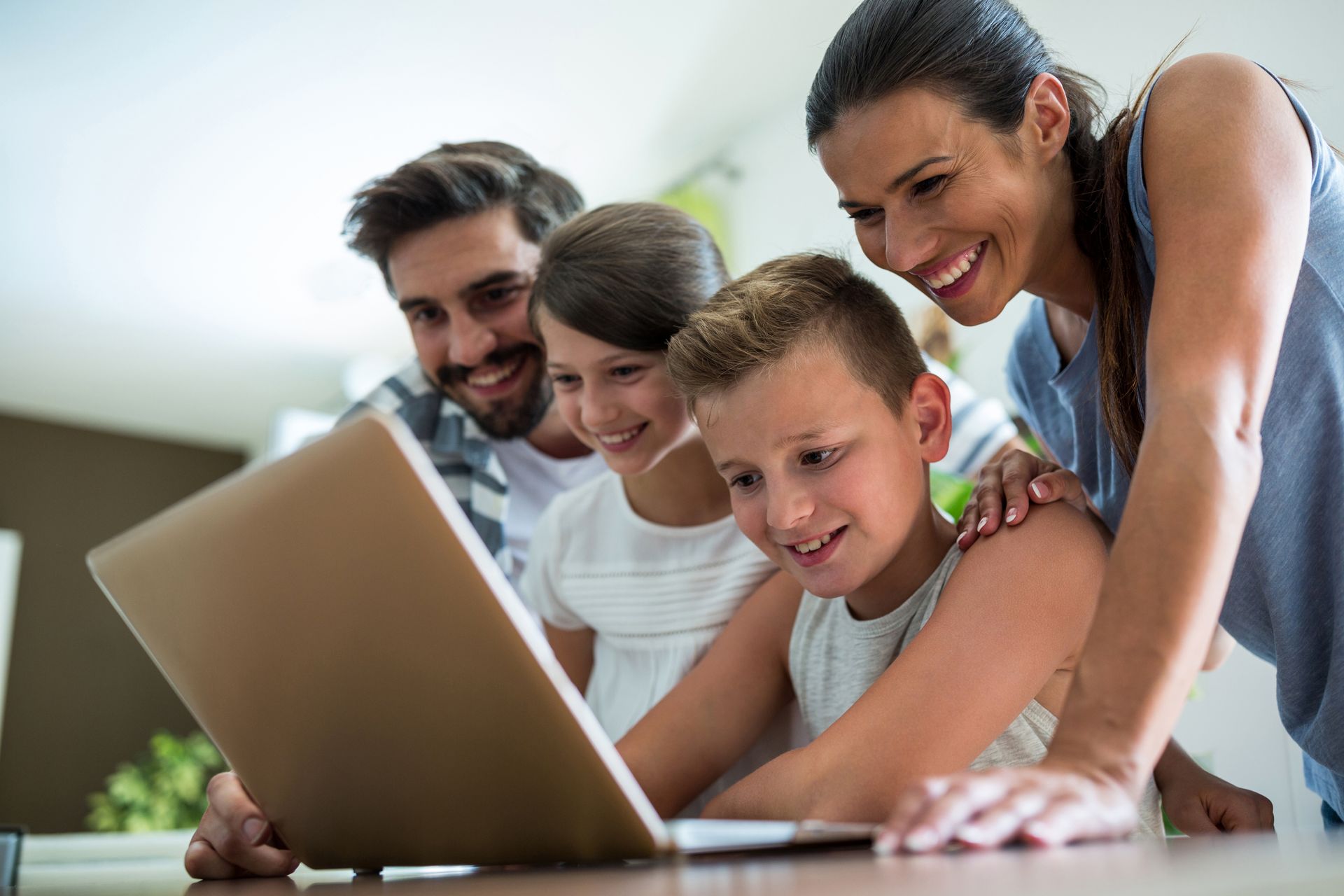 Family gathered around a laptop, smiling and looking at the screen together