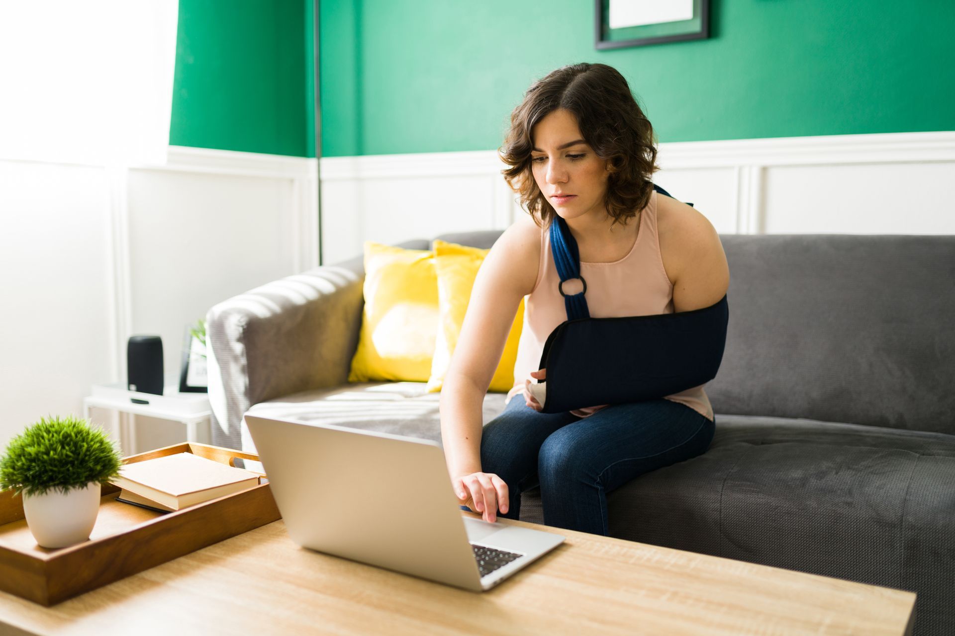 Woman using a laptop on a couch in a bright living room with green walls.