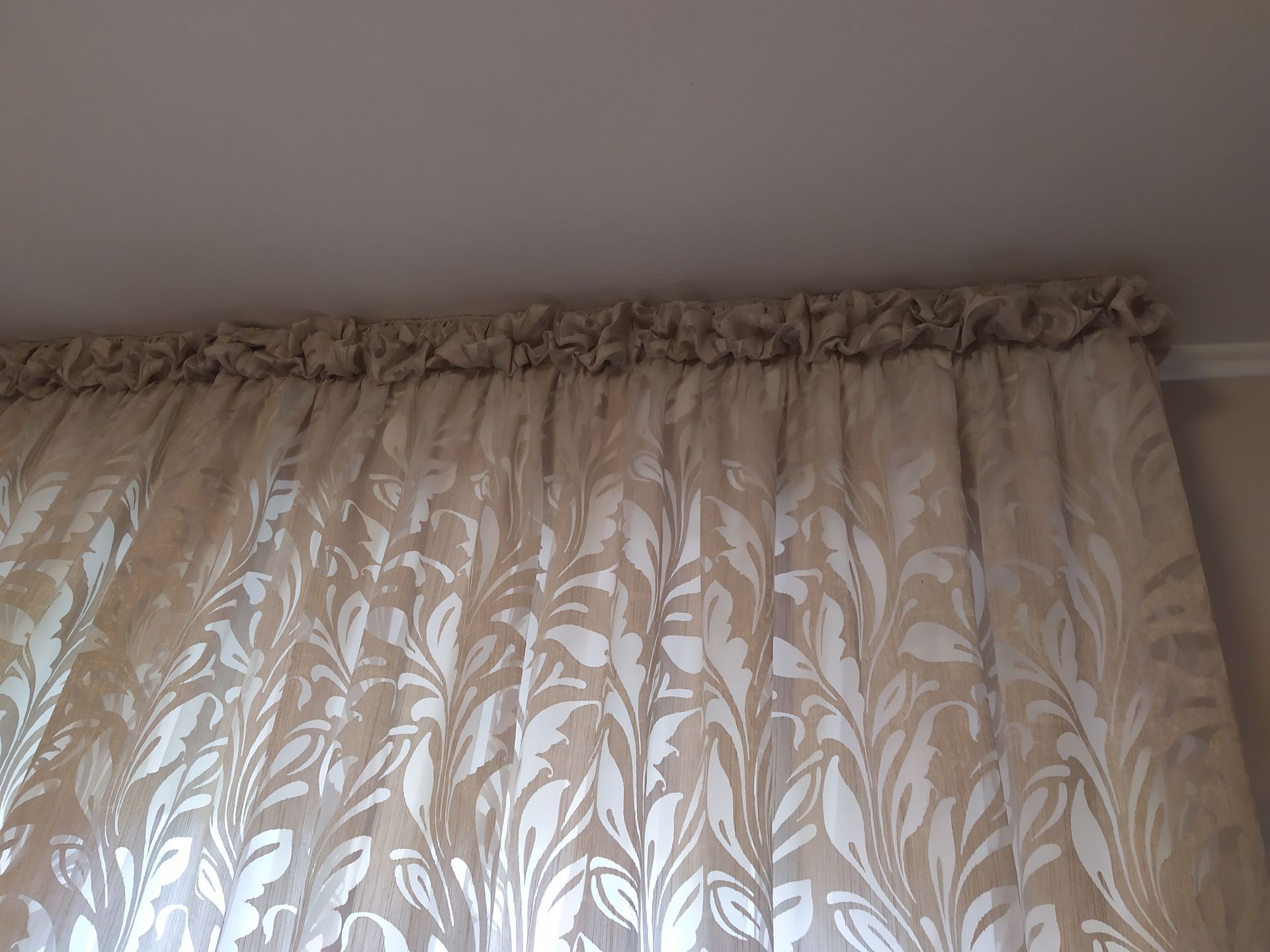 Una tenda con una balza superiore e un motivo ripetuto di foglie bianche e beige, appesa a un'asta sul soffitto.