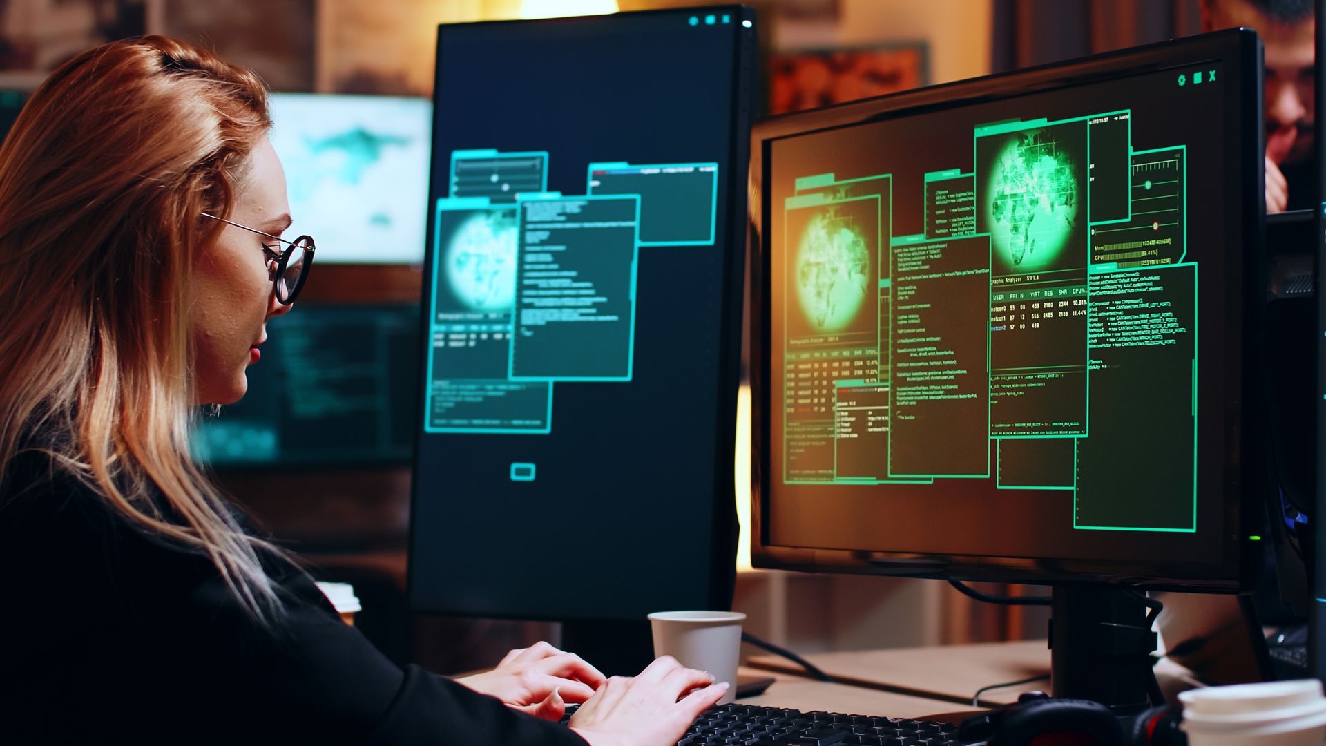 A woman is typing on a keyboard in front of two computer monitors.