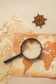 A magnifying glass rests on an antique world map next to a small wooden ship's wheel.