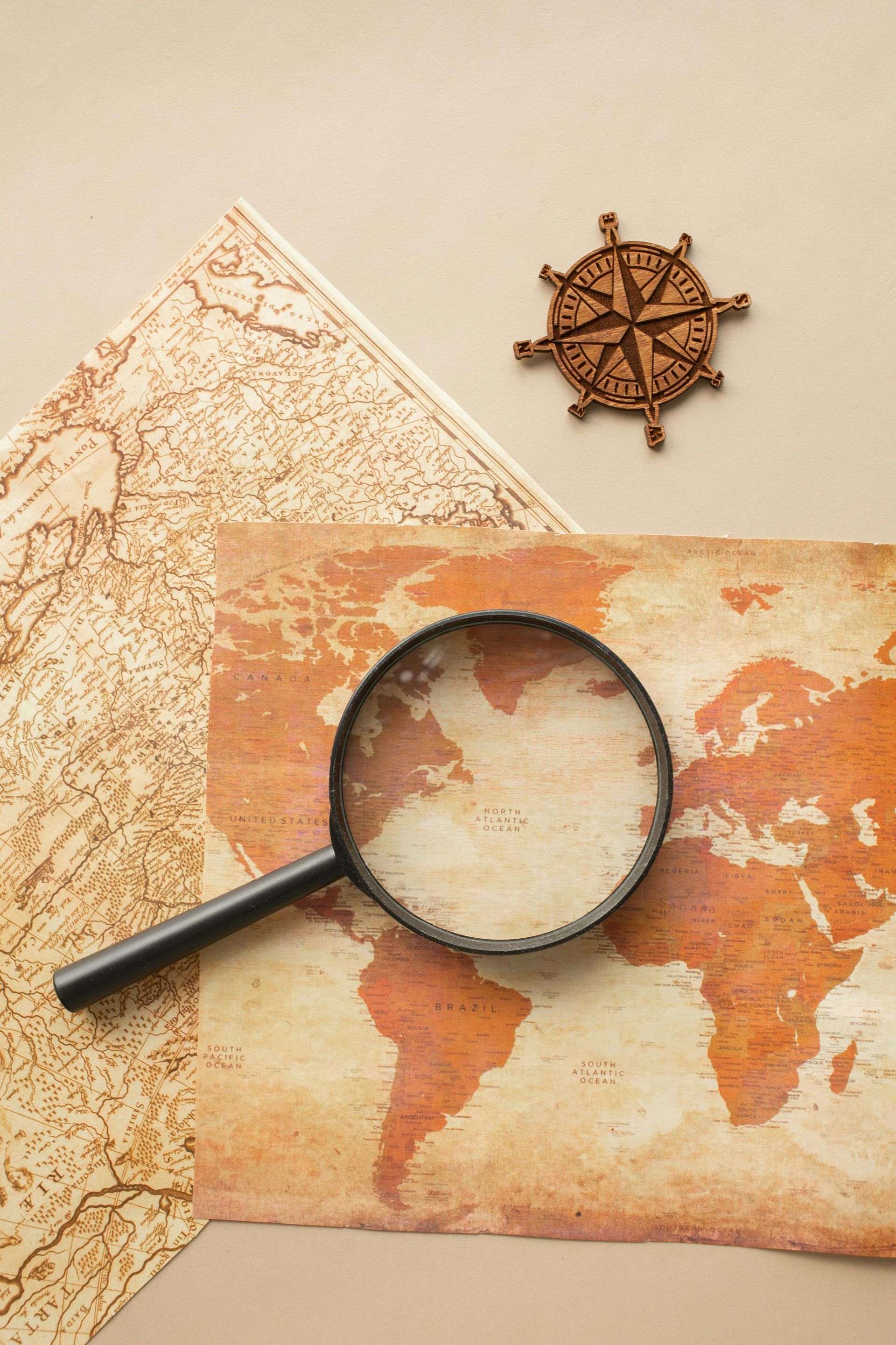 A magnifying glass rests on an antique world map next to a small wooden ship's wheel.