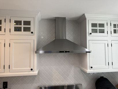Stainless steel range hood centered between white kitchen cabinets. White tile backsplash.