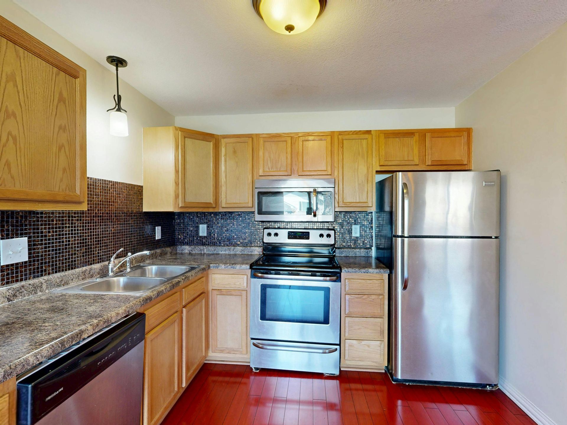 Small kitchen with wood cabinets, stainless steel appliances, granite counters, and a tiled backsplash.