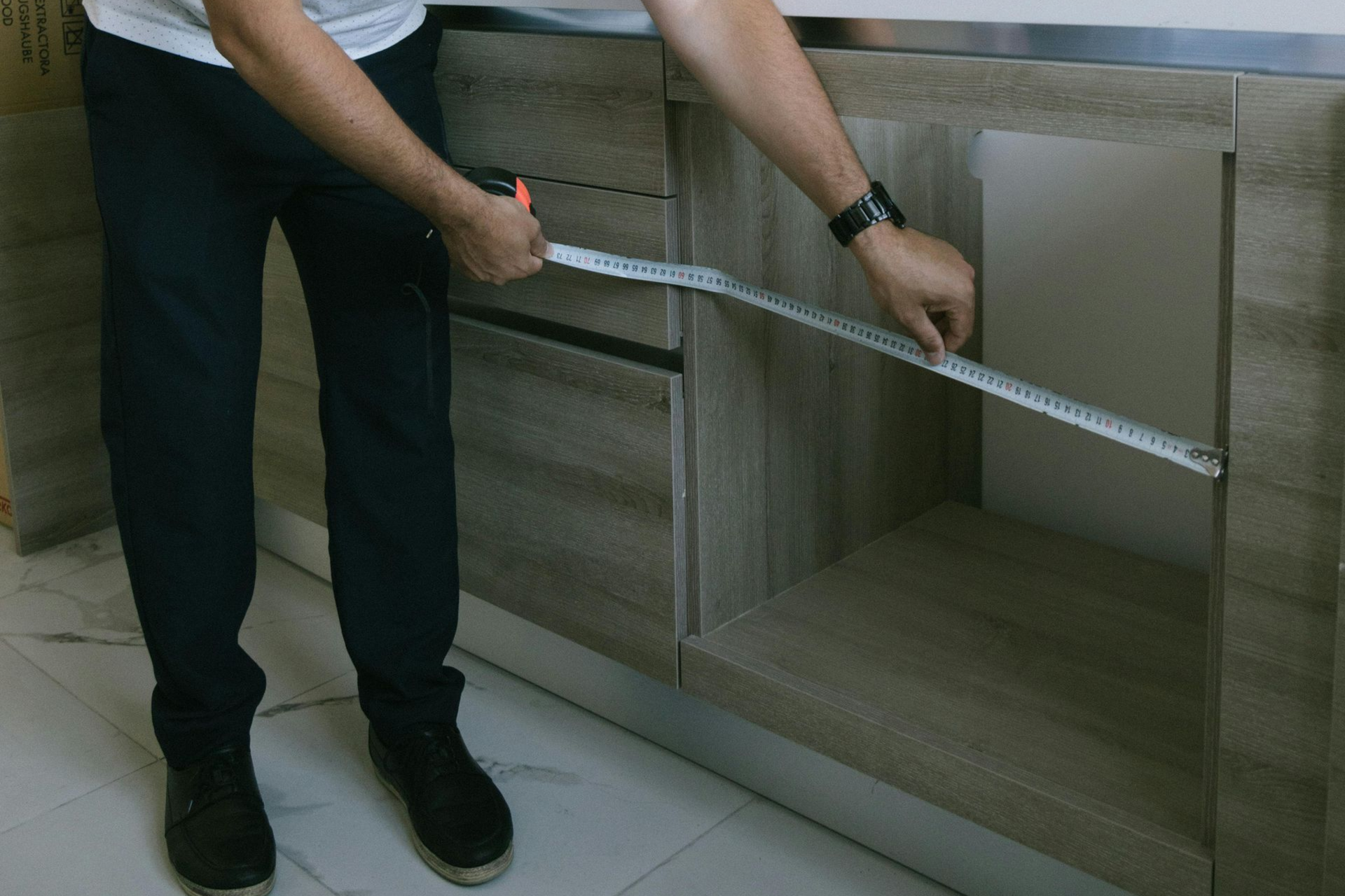 Person measuring the width of a kitchen cabinet with a tape measure