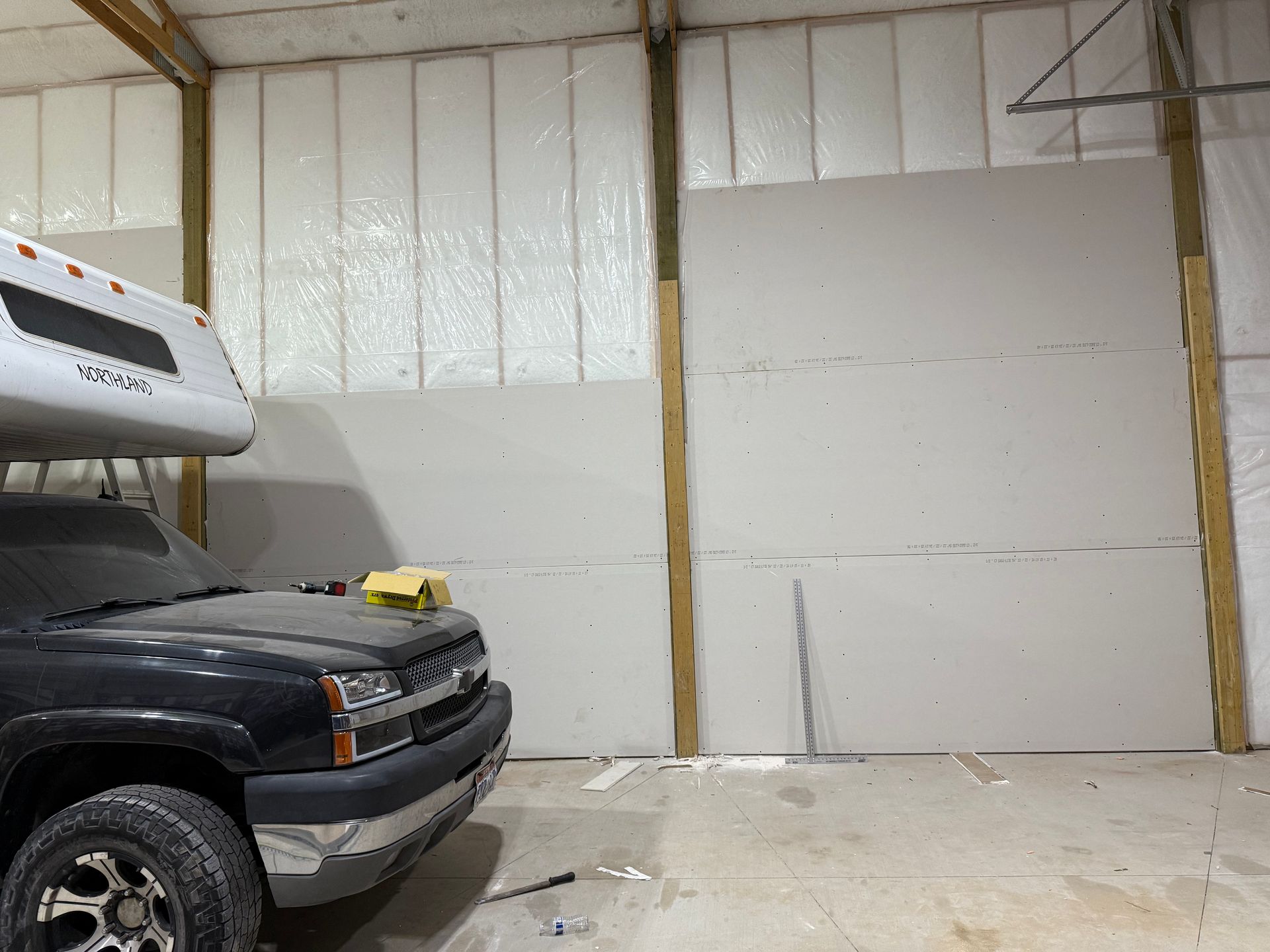 A truck is parked in a work garage with a camper on top of it.