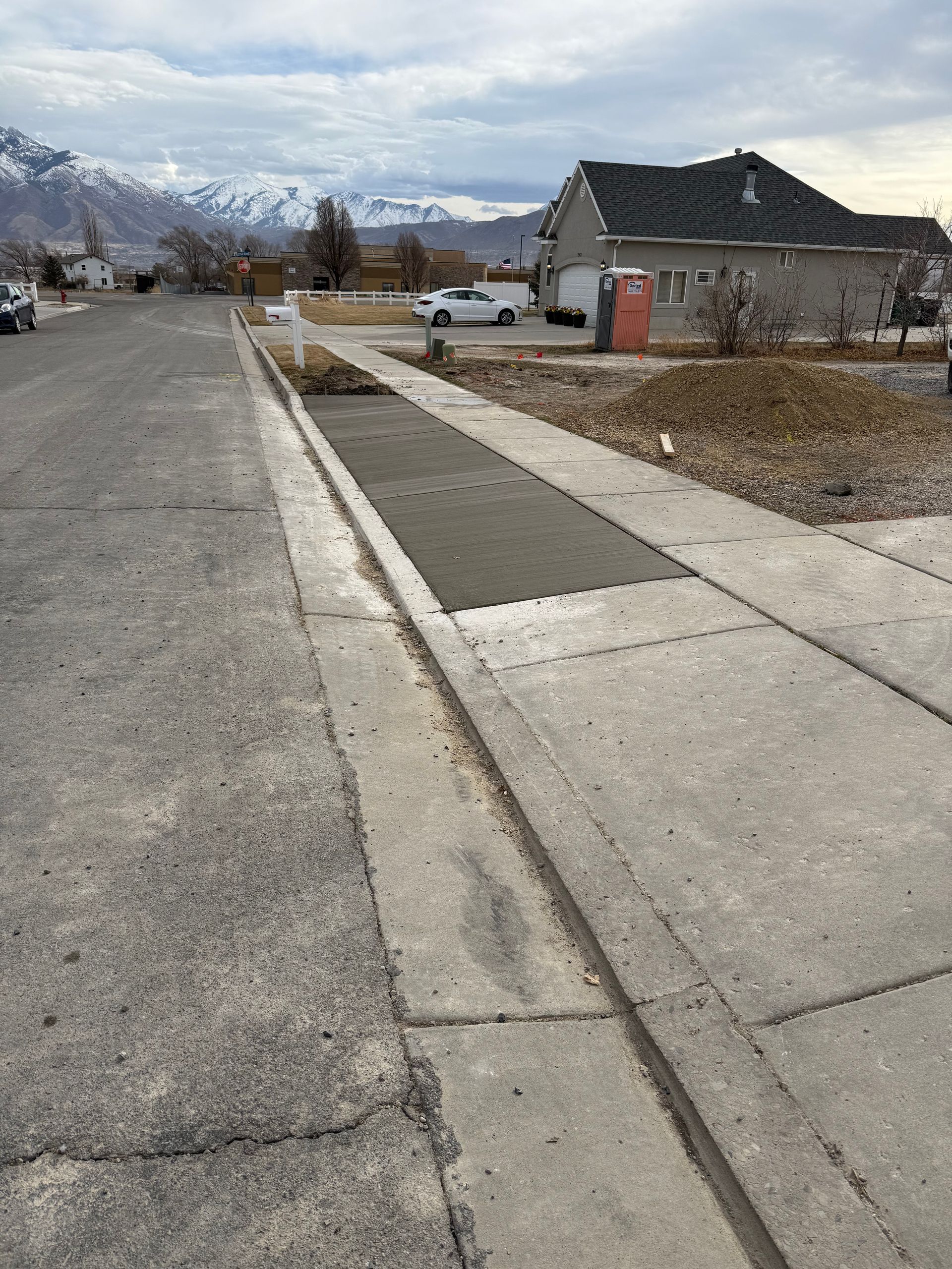 A new concrete sidewalk along a street with a house in the background