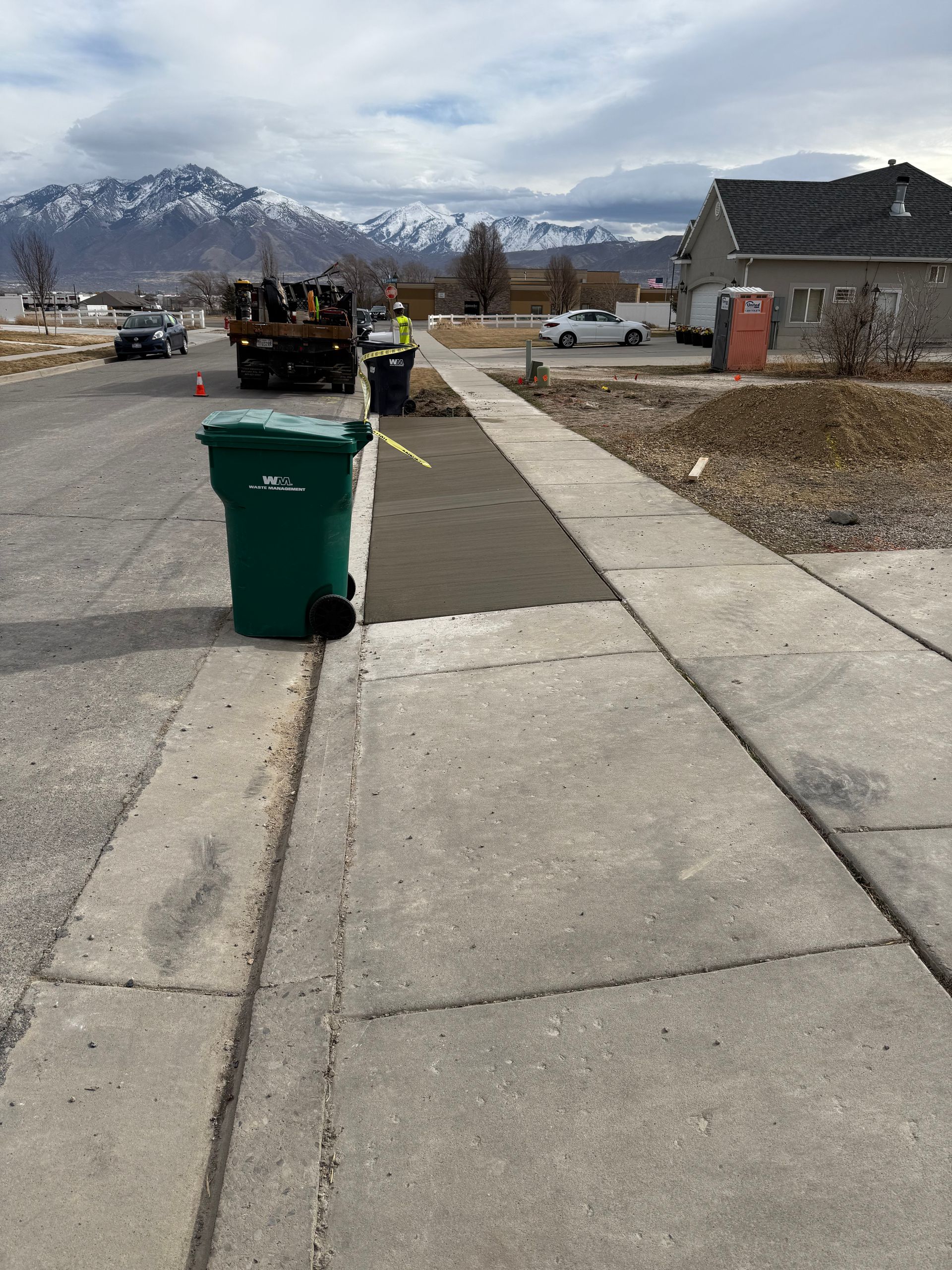 A recently poured sidewalk next to a truck and garbage can.