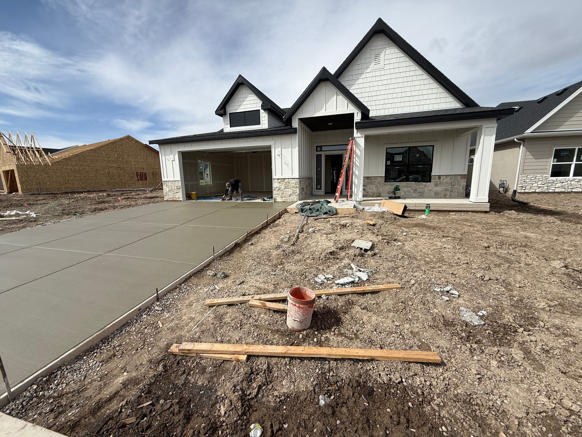 A house under construction with a newly poured concrete driveway in front of it.