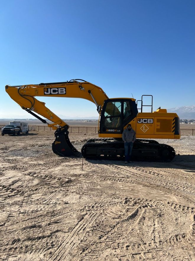 A yellow jcb excavator is parked in the middle of a dirt field.