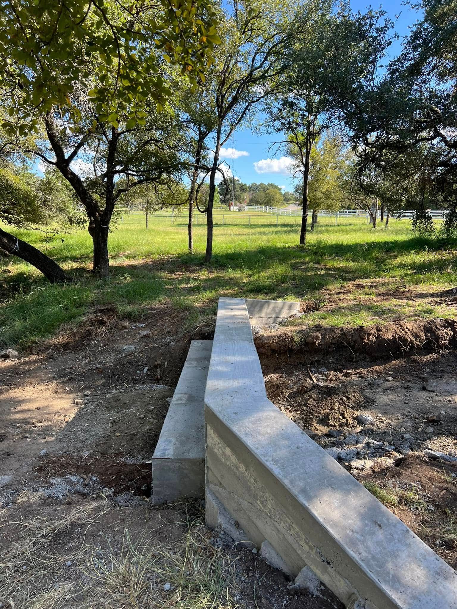 A concrete bench is sitting in the middle of a field with trees in the background.