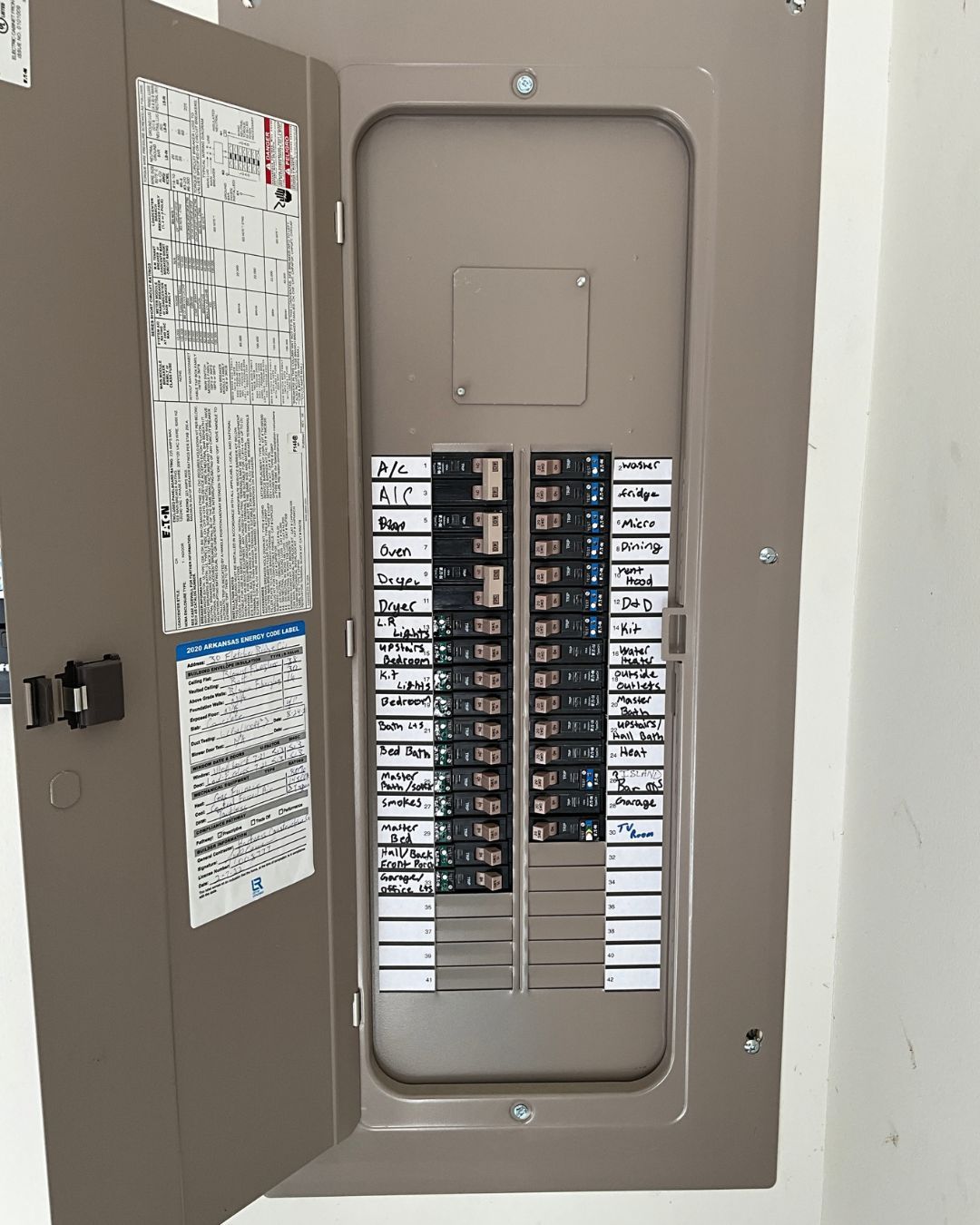 Open electrical breaker panel with rows of black circuit breakers and exposed wiring.