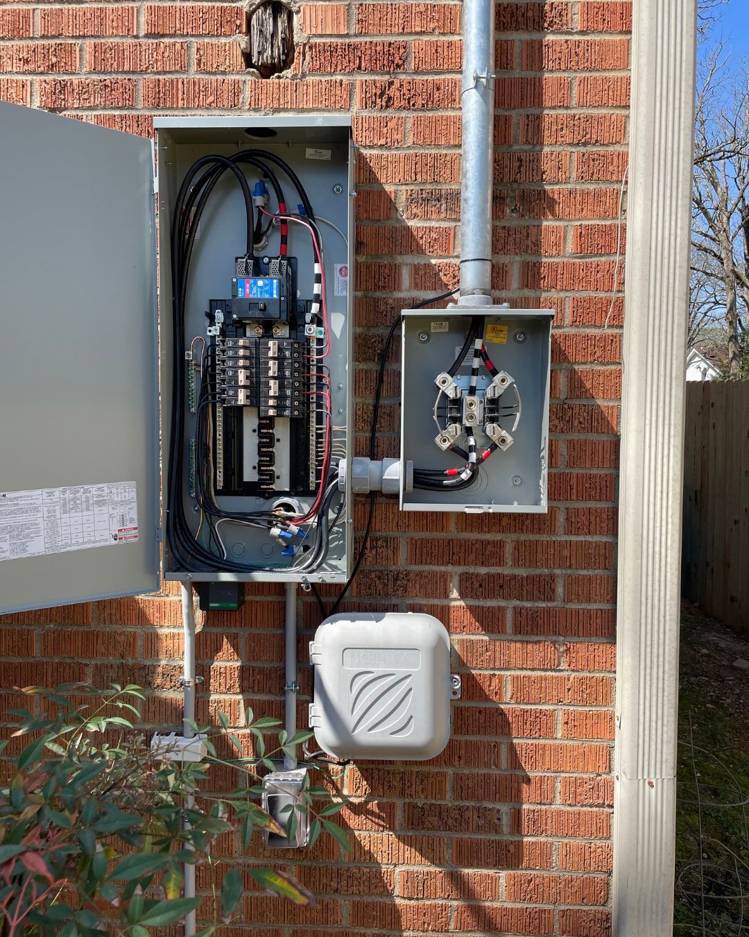 Open electrical panel on a brick house exterior with wiring and a surge protector.