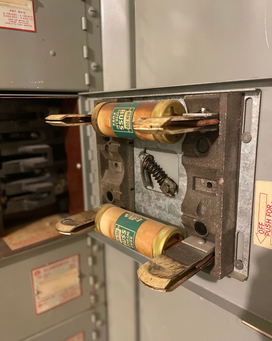 Open electrical panel with breaker switches and exposed wiring on a gray metal door
