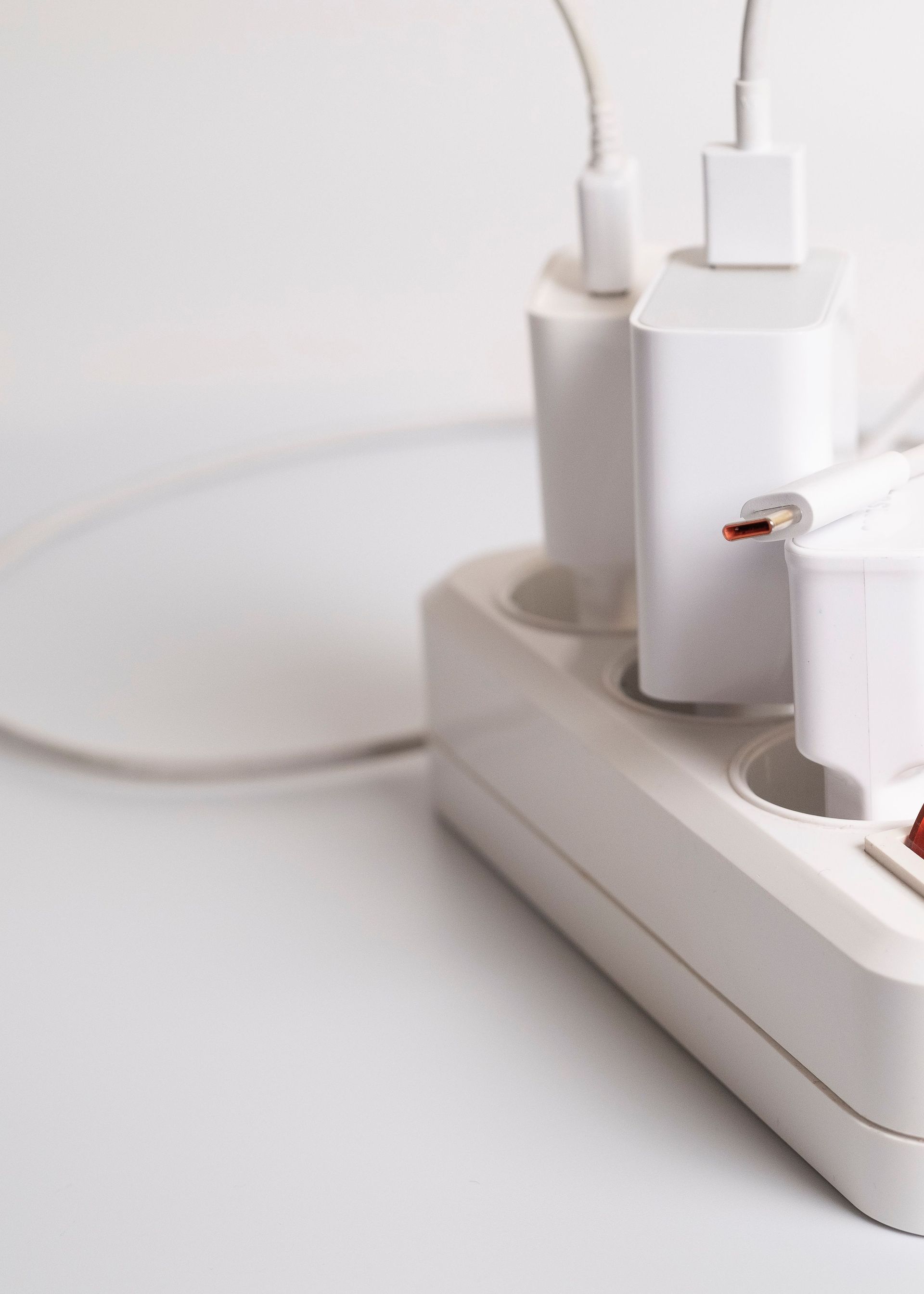 White power strip with multiple plugged-in chargers and cables on a white surface