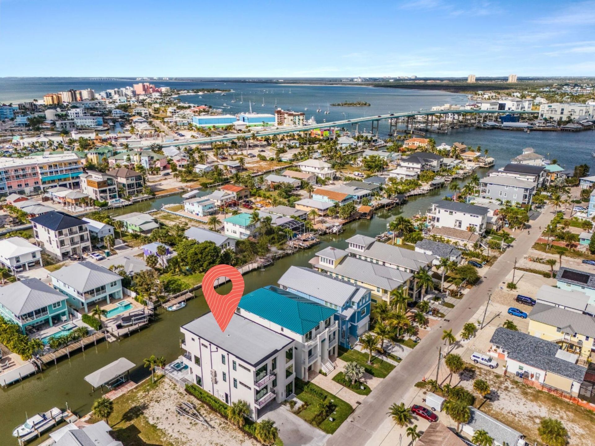 Aerial view of a coastal neighborhood with canals, marina, and a red map pin on a white building with a blue roof
