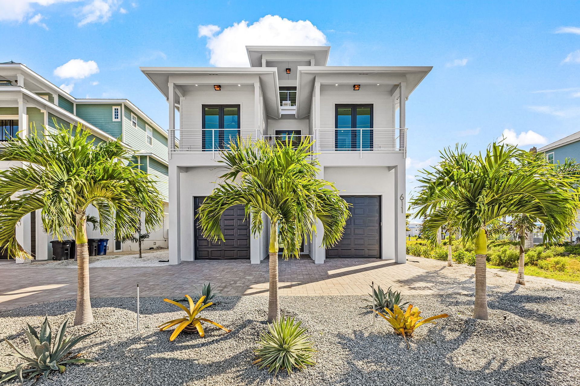Modern two-story white house with palm trees and a gravel front yard under a bright blue sky