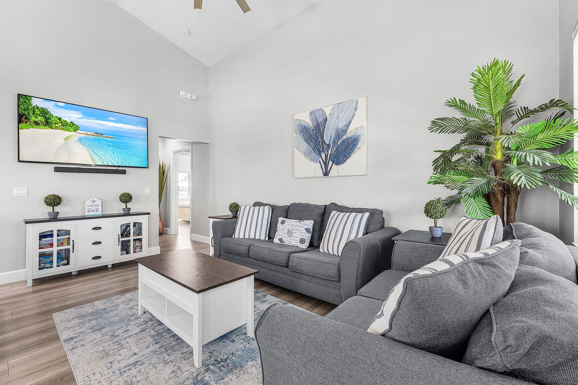 Bright living room with gray sofas, white coffee table, TV, and large potted plant