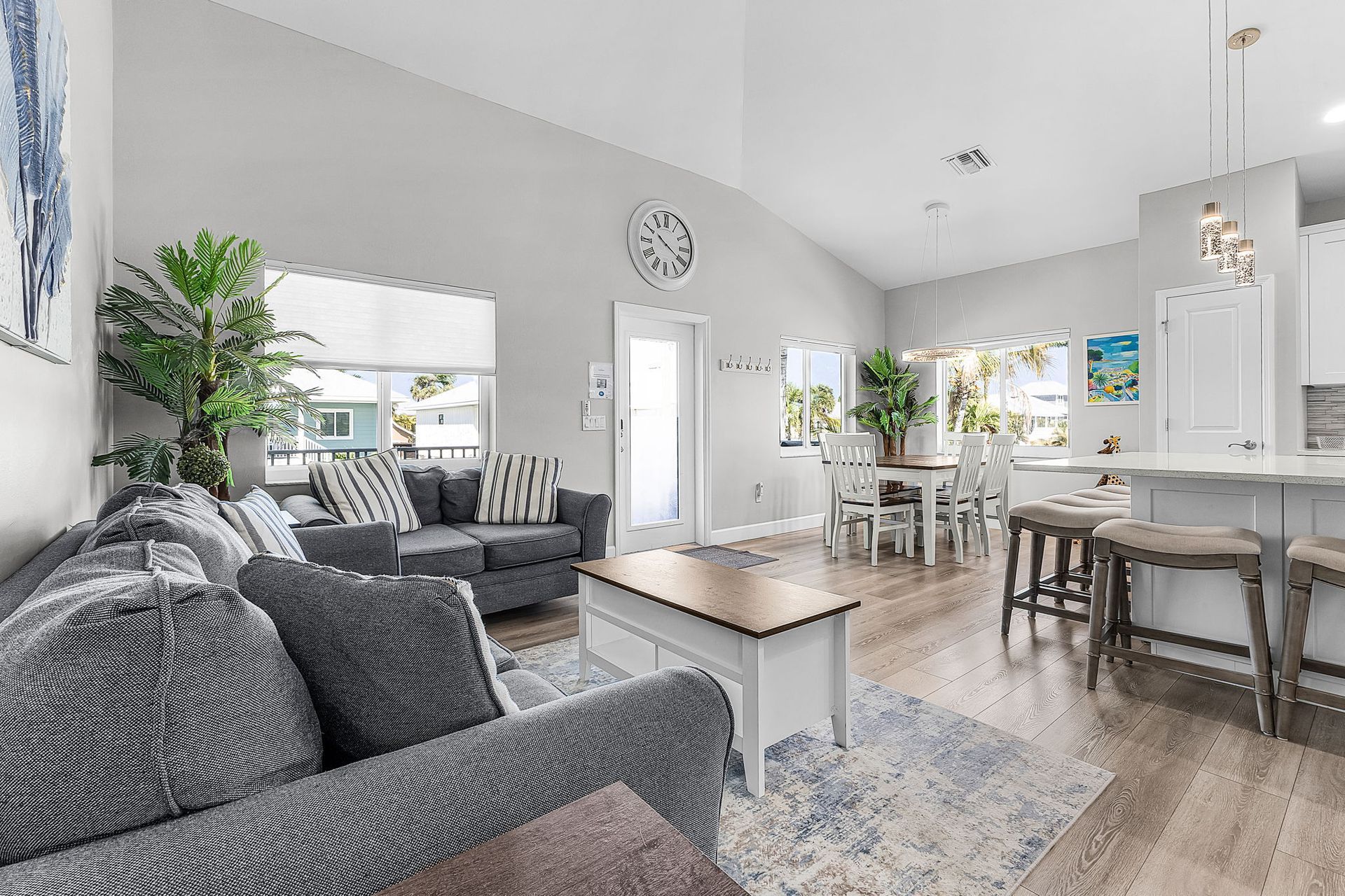 Bright open-plan living room with gray sofas, white walls, a dining area, and kitchen island.