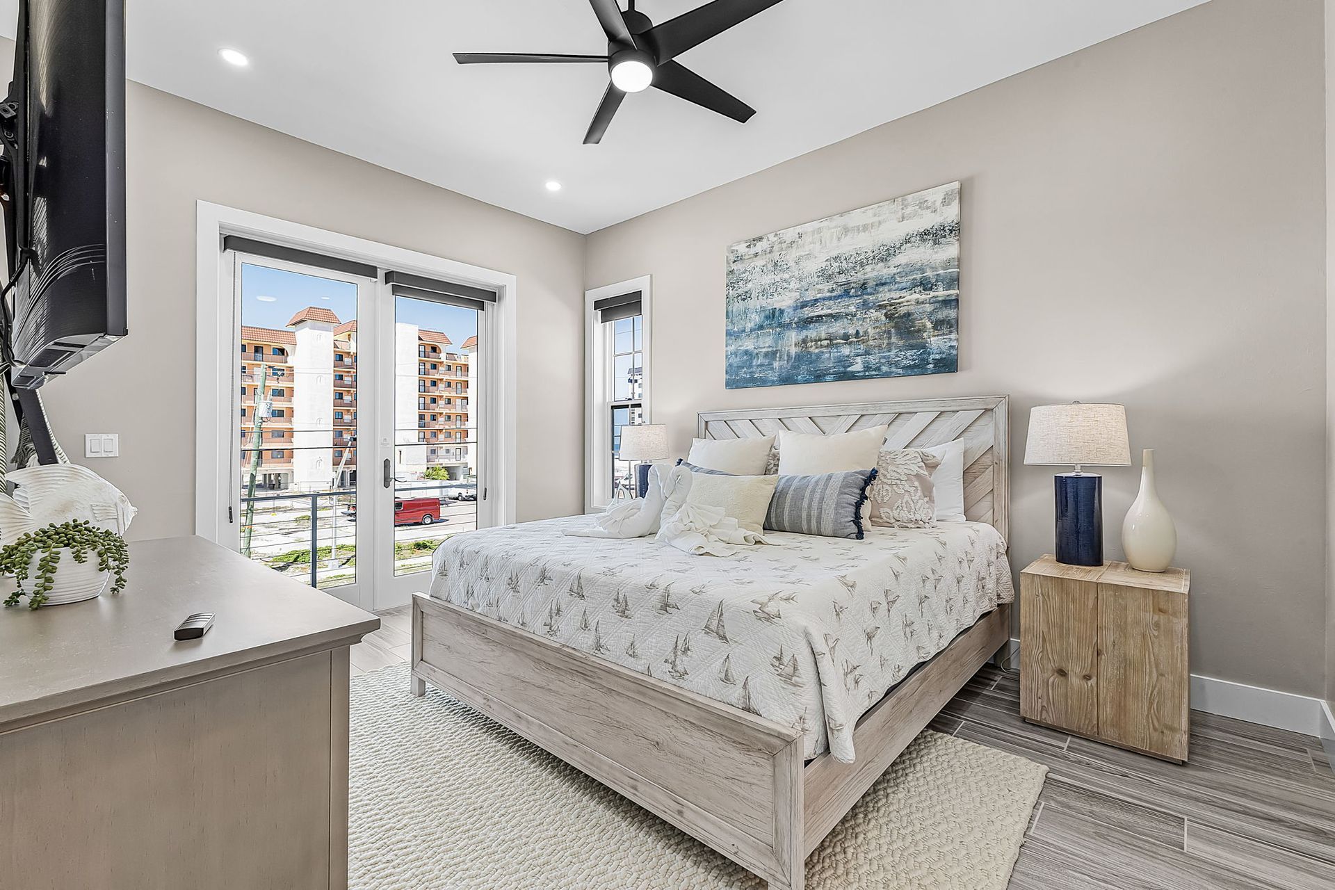 Bright modern bedroom with a bed, large windows, ceiling fan, and neutral decor