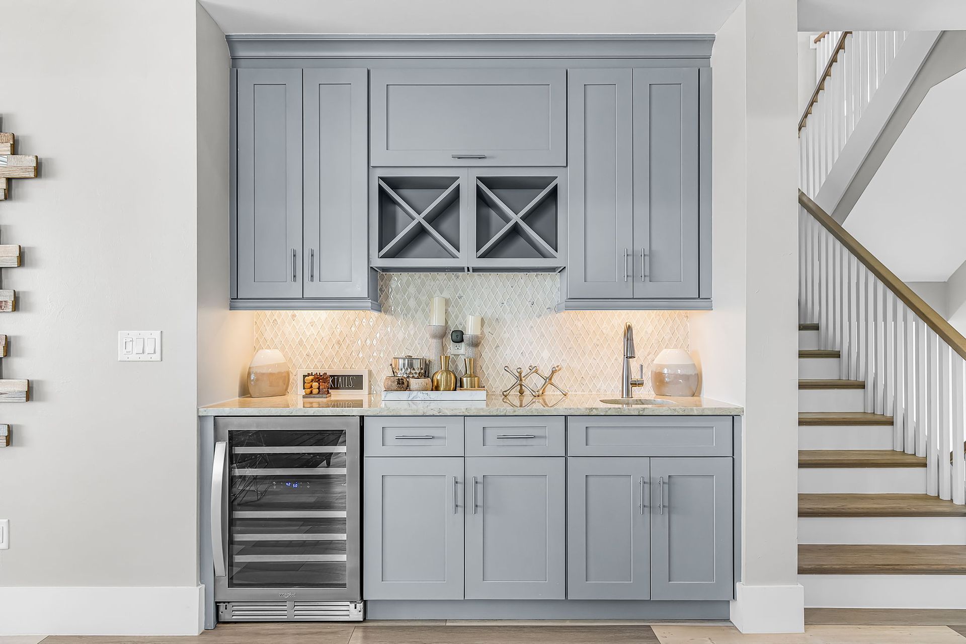 Built-in gray bar nook with wine fridge, cabinets, and staircase beside it