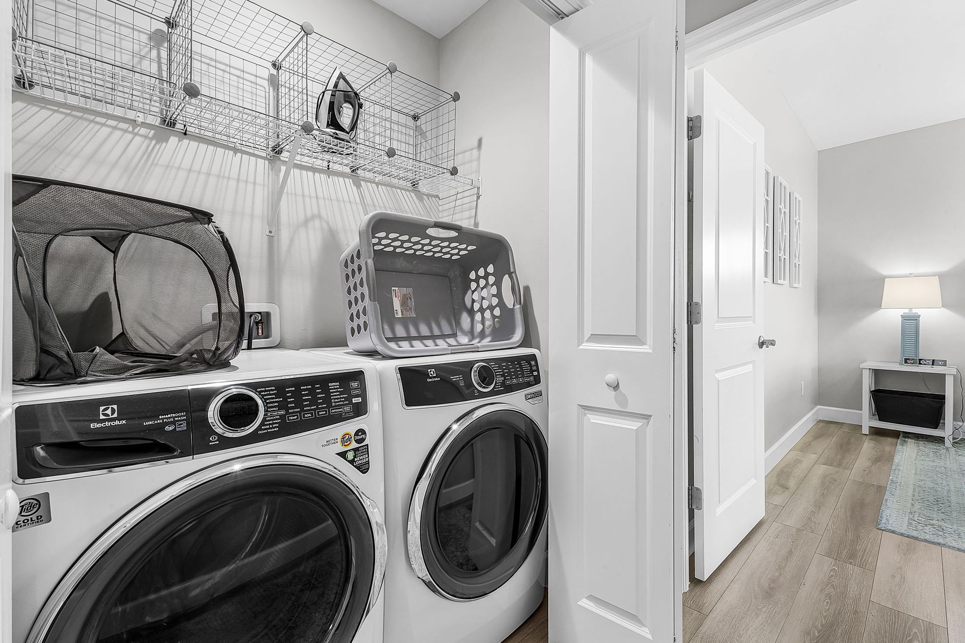 Laundry room with washer and dryer, wire shelf above, and open door to a bright hallway