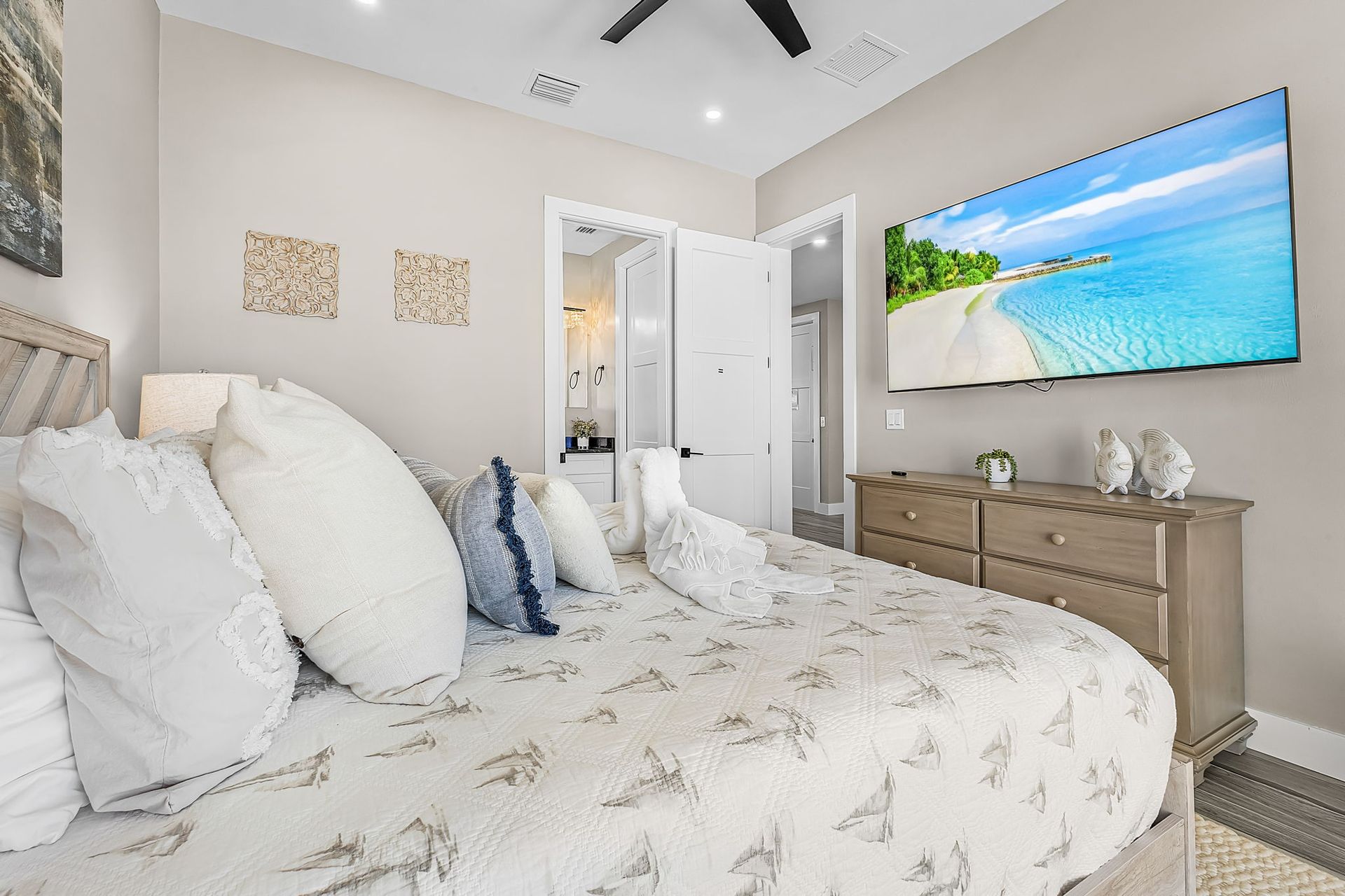 Bright bedroom with white bedding, gray walls, and a wall-mounted beach scene above a dresser.