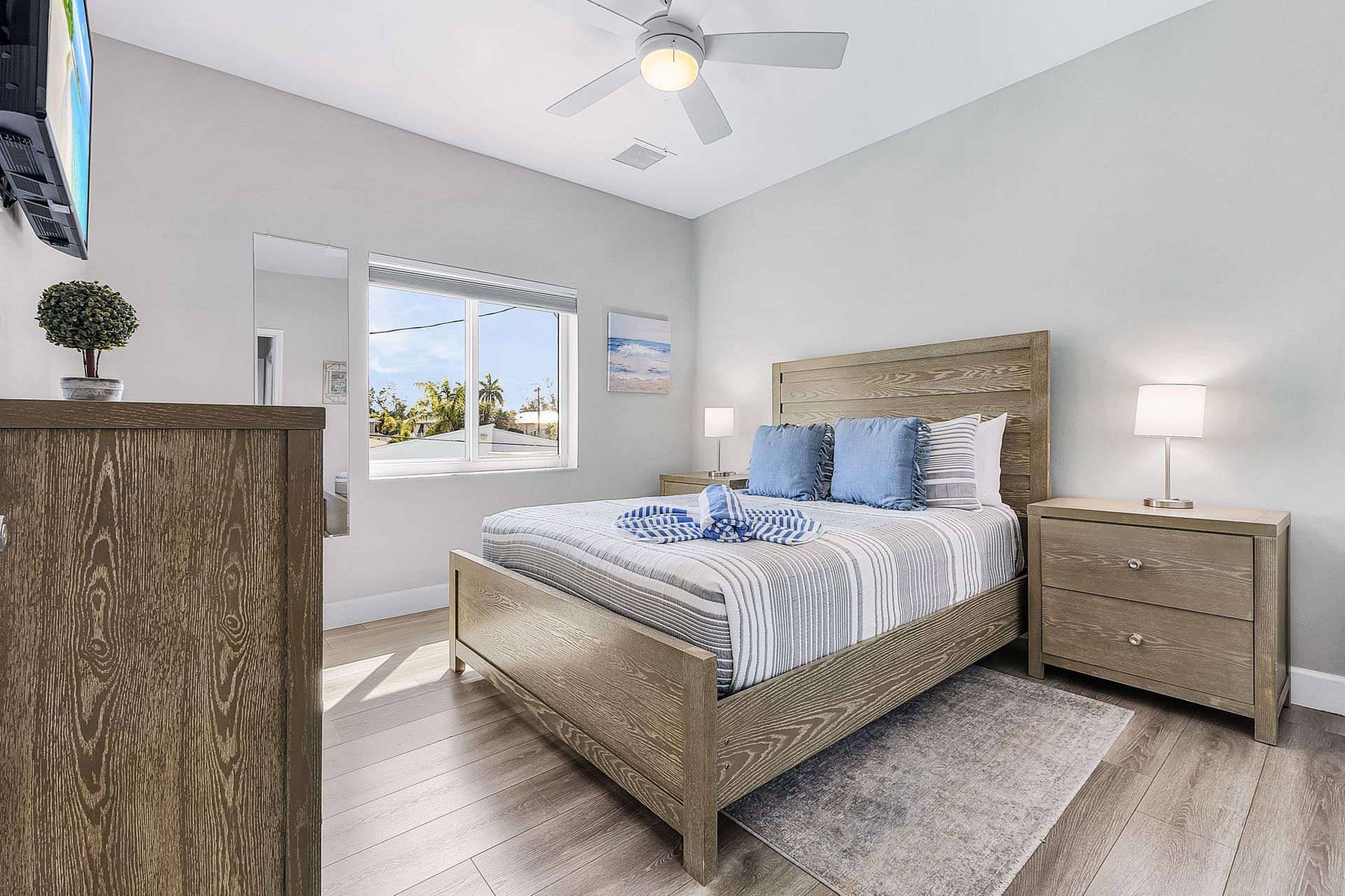 Bright bedroom with a wooden bed, nightstand, dresser, and window with daylight.