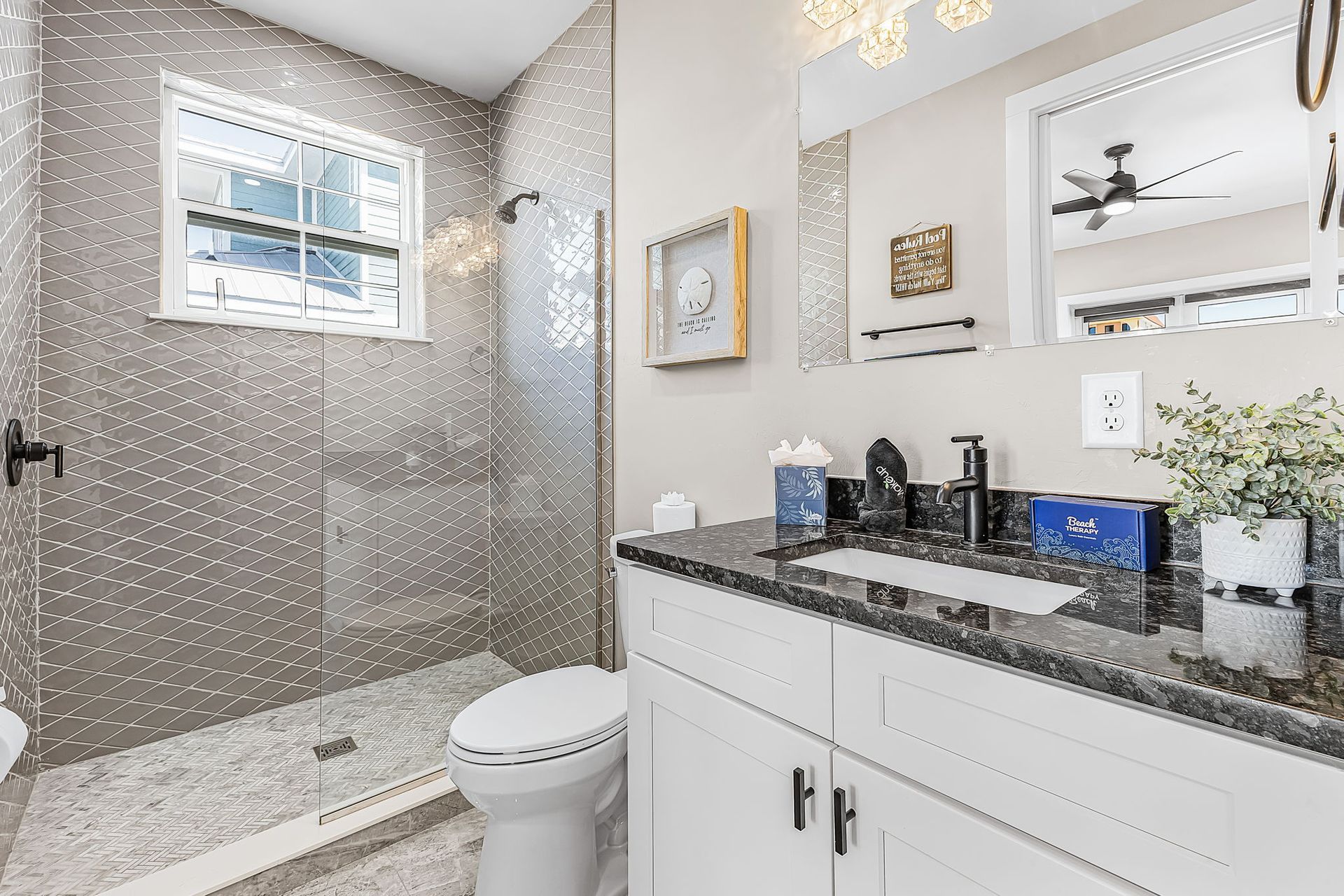 Modern bathroom with glass shower, granite vanity, toilet, and gray tile walls