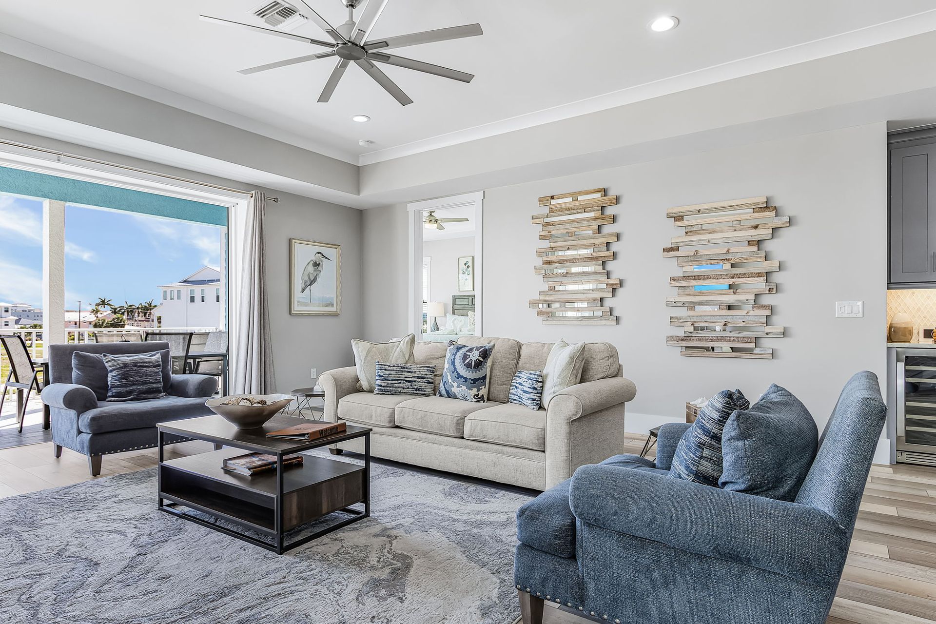 Bright modern living room with gray sofas, blue chair, coffee table, and large windows overlooking water