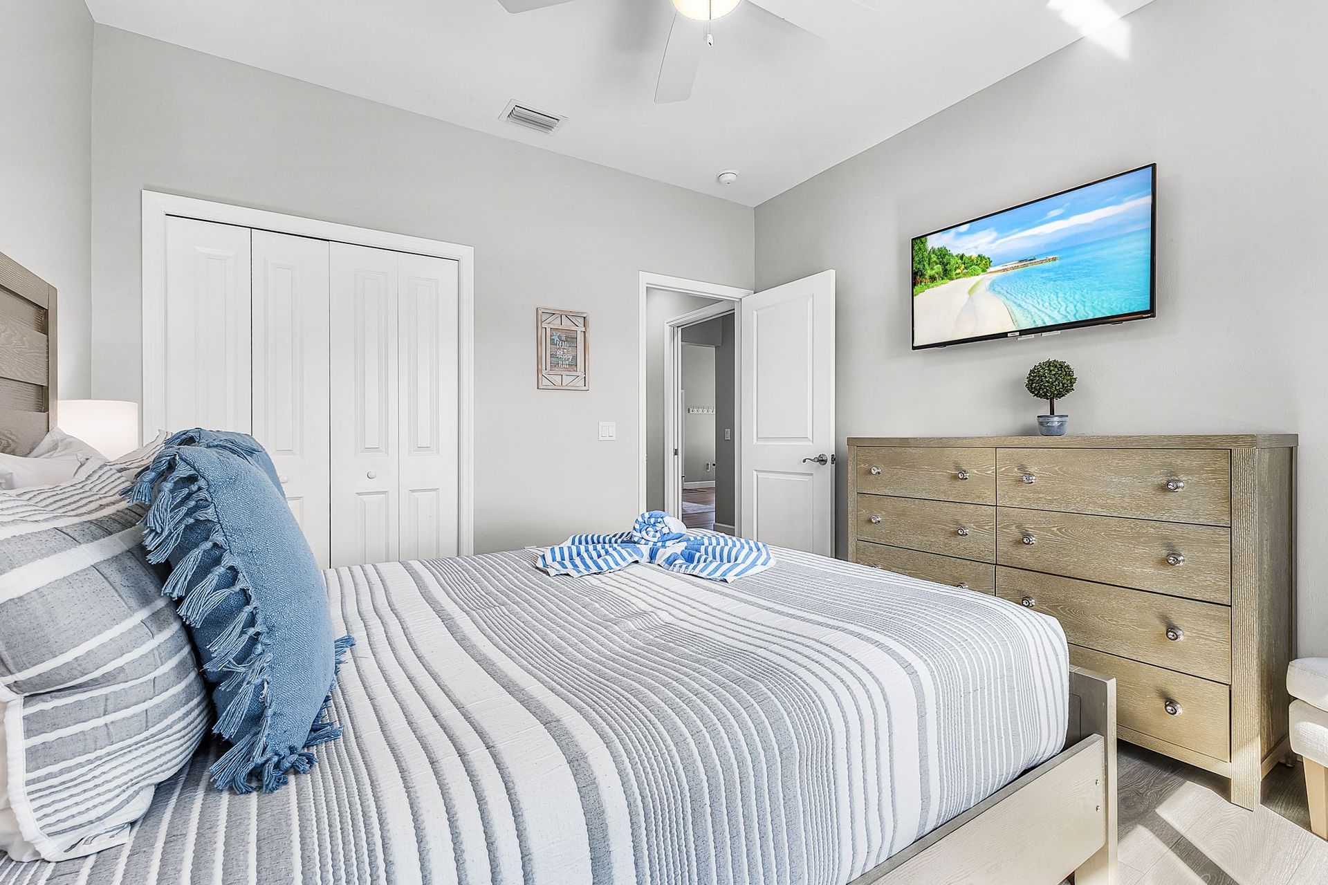 Bright bedroom with a striped bed, white closet doors, and a dresser with a wall-mounted TV.