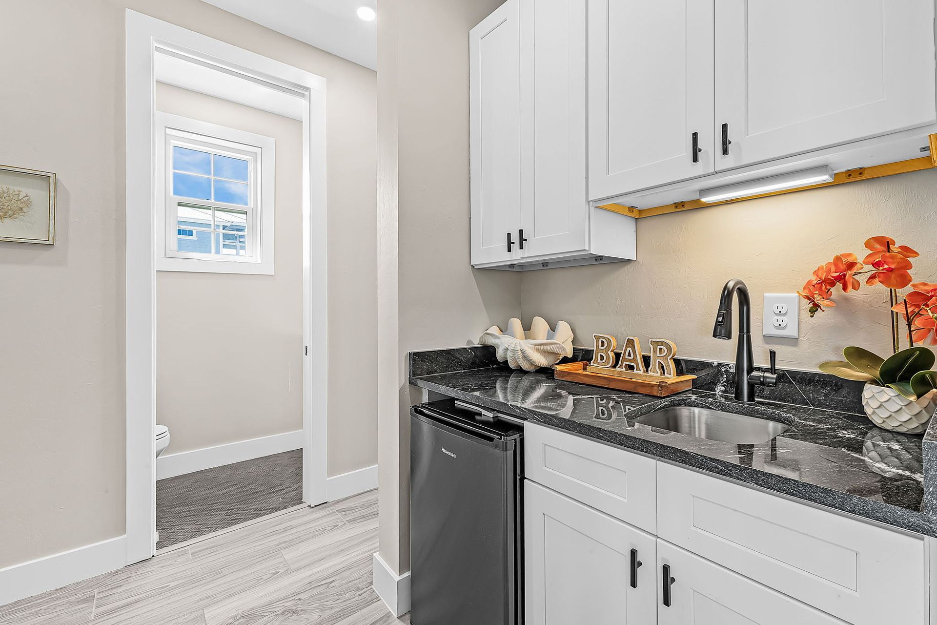 Bright white kitchen with granite counter, black appliances, and doorway to a carpeted room